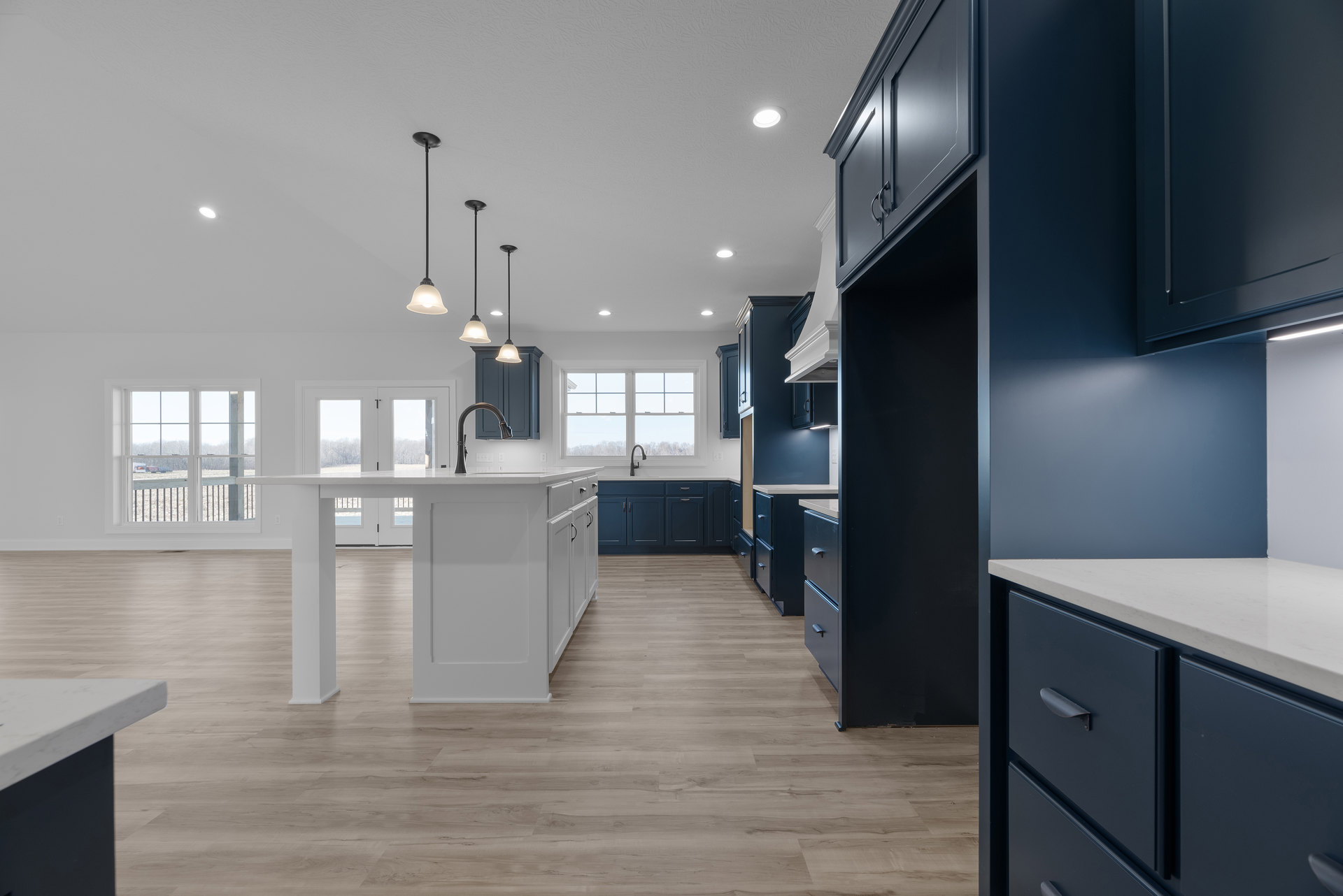 Blue kitchen cabinets with brushed metal hardware, wood plank flooring, white walls, stone countertop, modern pendant light fixture, stainless steel sink, and built-in drawers.