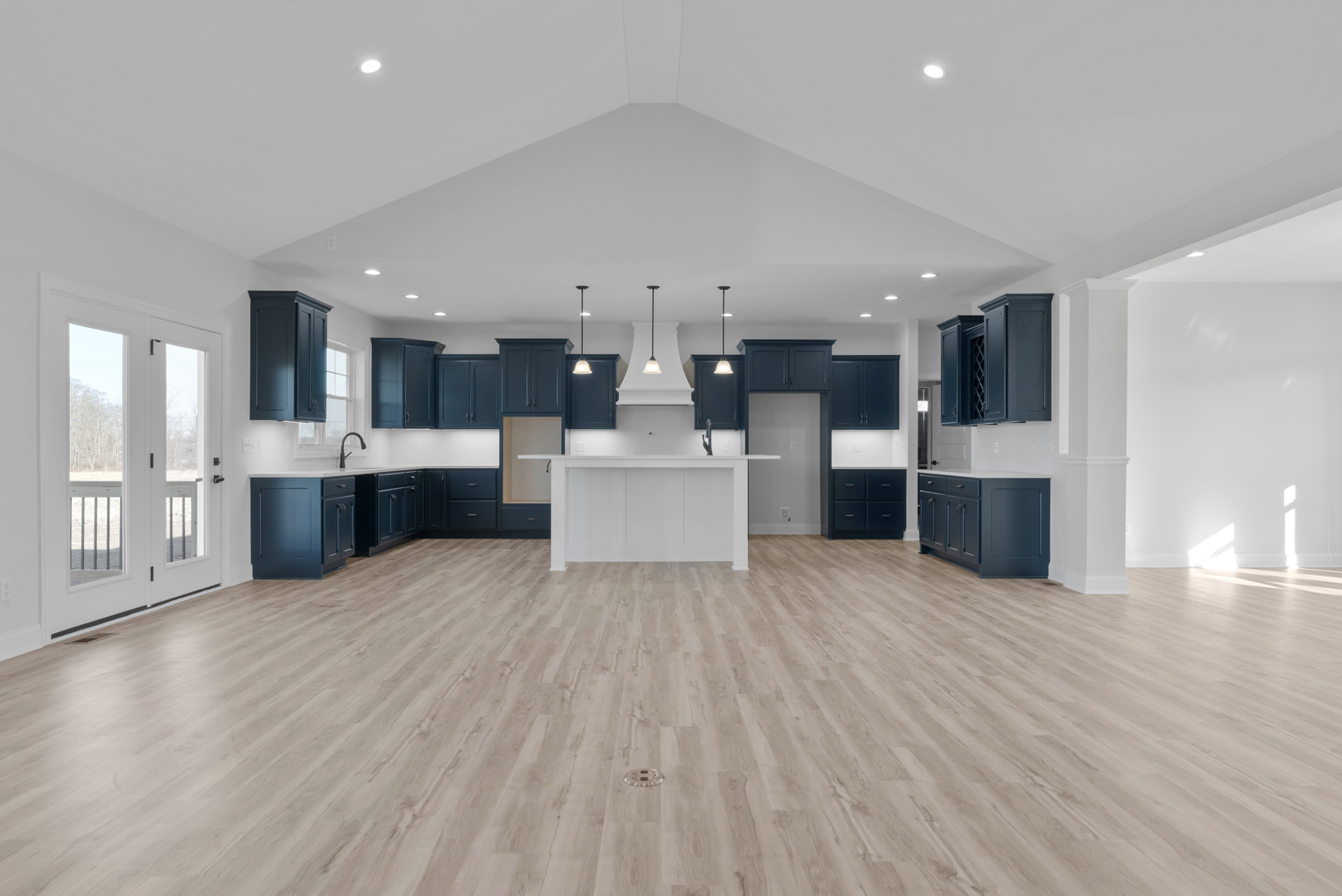 Spacious kitchen with blue cabinets, white countertops, wood flooring, blue island with black handles, white table, and glass door opening to balcony with trees