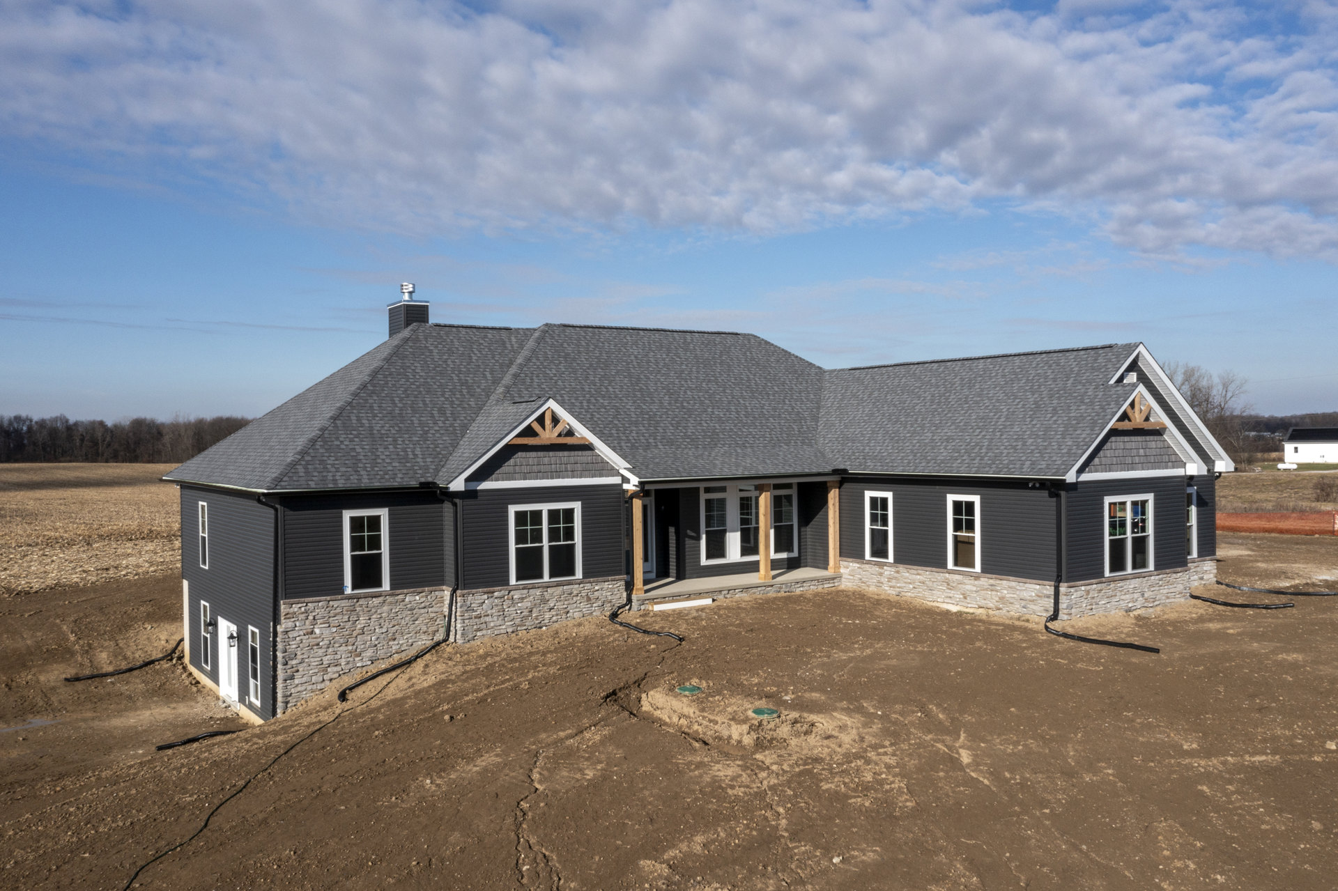 Modern house with white-framed windows, gray roof, and brick chimney, set on a dirt hill under a cloudy sky