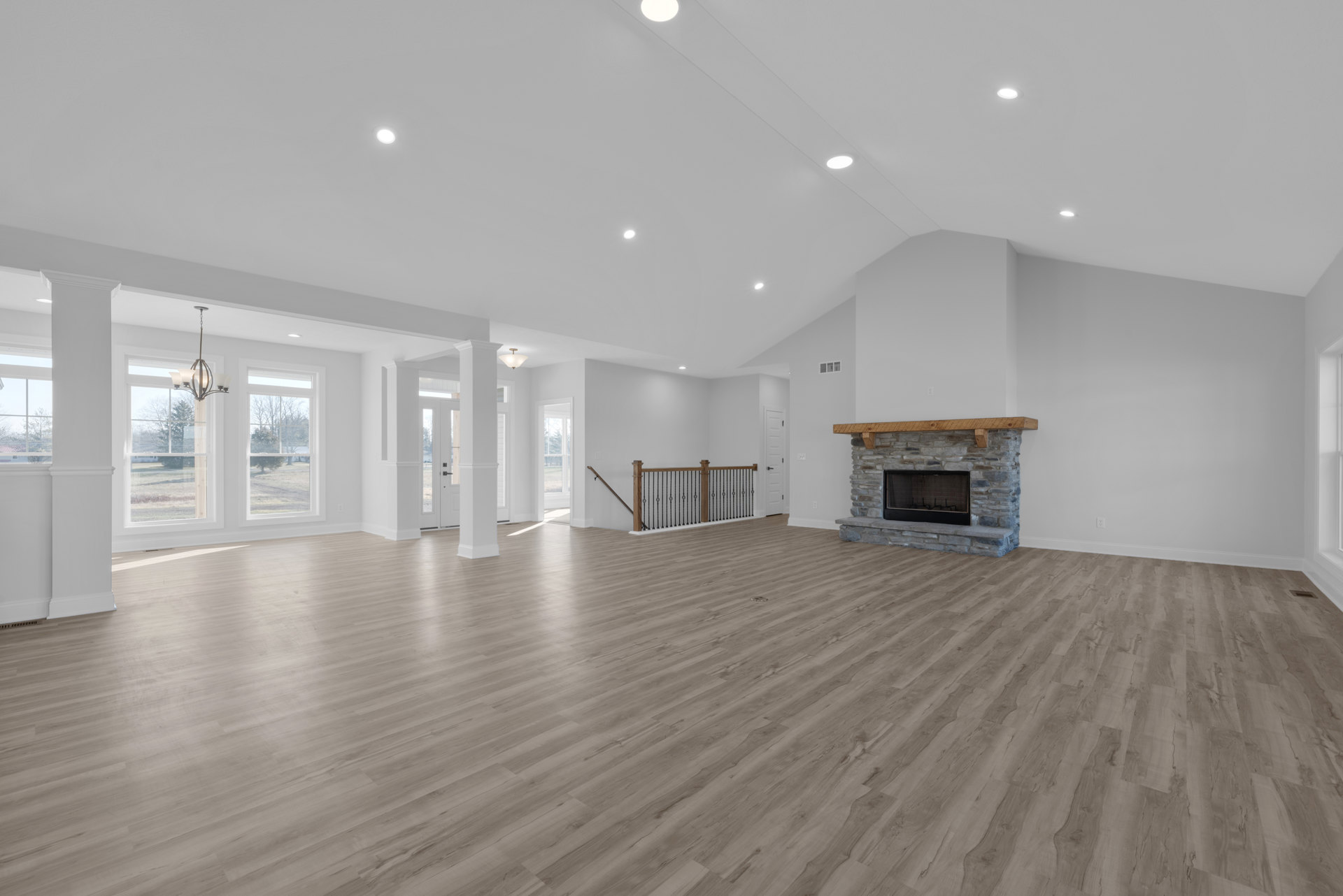 Spacious living area featuring hardwood floors, plaster walls, wood beam mantel above a glass-door fireplace, and metal railing