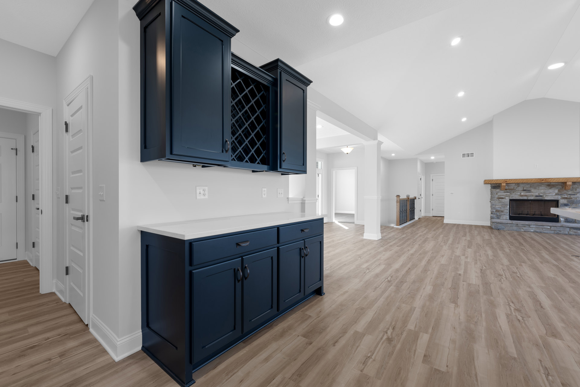 Kitchen with blue cabinets, white countertops, wood flooring, built-in wine rack, and a fireplace featuring a wood mantel shelf.