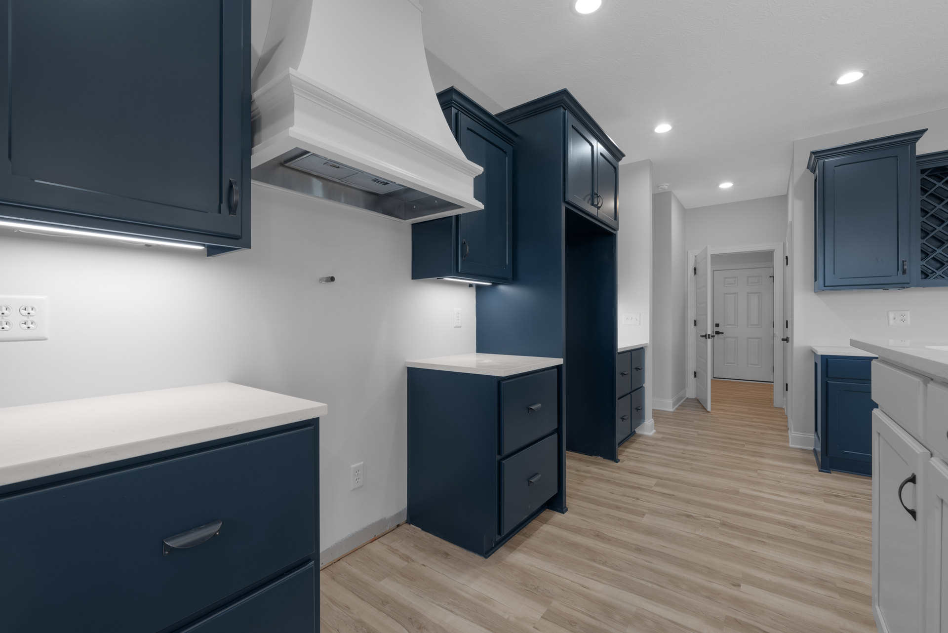 Blue kitchen cabinets with white countertops, white walls, black hardware, and wood flooring