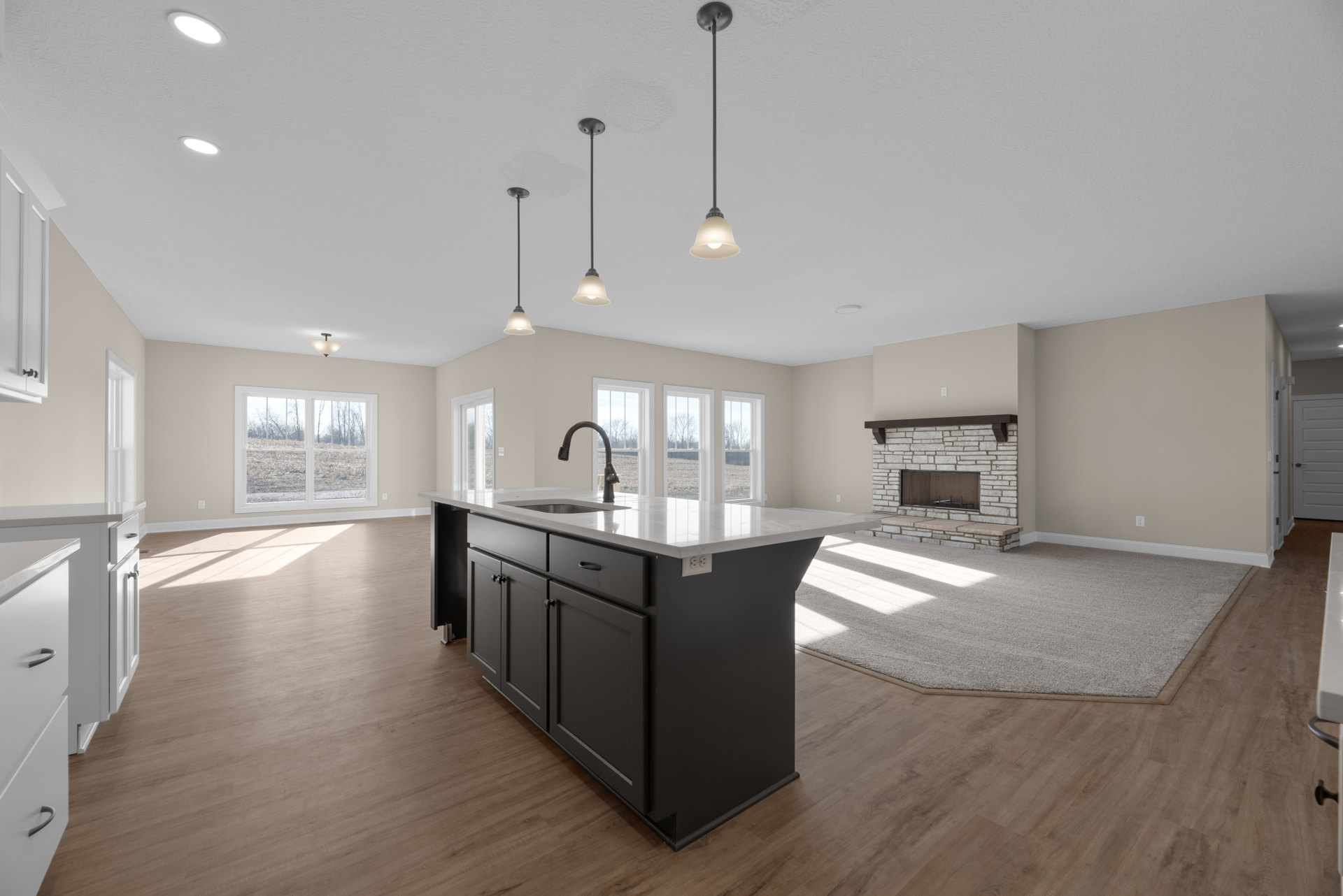 Quartz kitchen island with built-in sink, white cabinetry, wood flooring, large window overlooking grassy field, modern fireplace with glass front, and smooth white walls