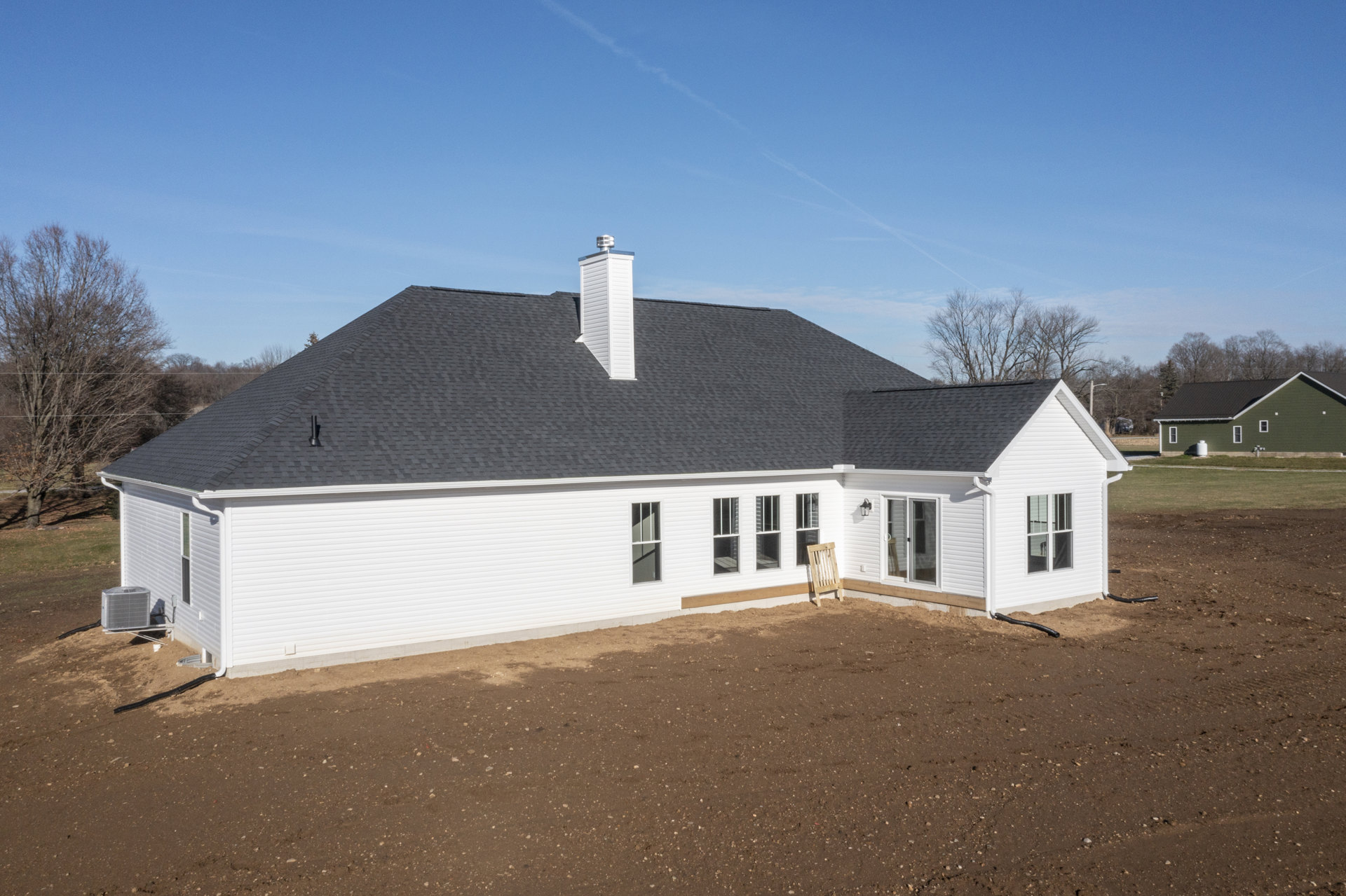 White house with black roof and white chimney, wooden chair against exterior wall, leafless trees in background