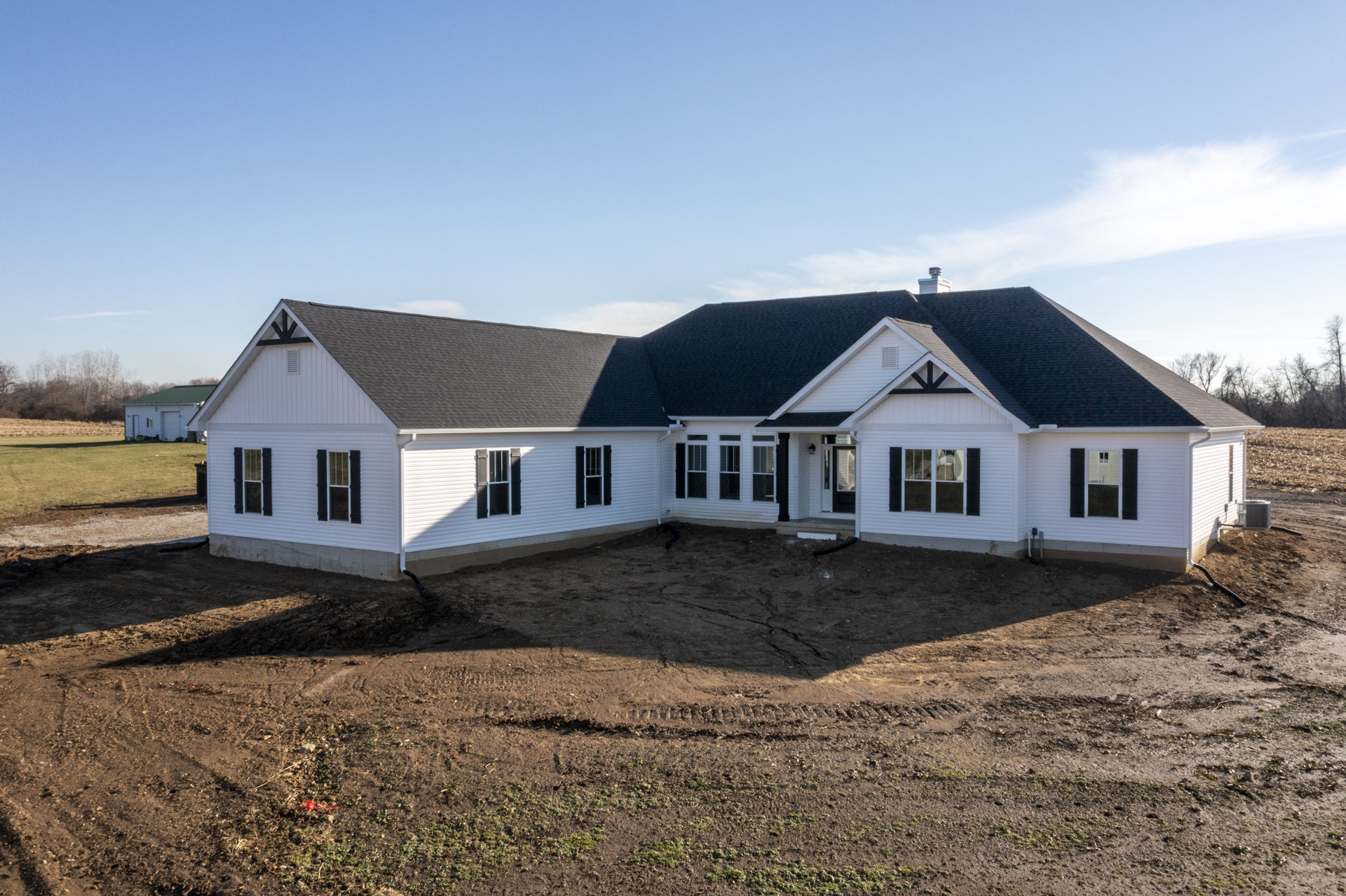 Partially built house with black shingle roof, white-framed windows, exposed dirt foundation, and black pipe on ground under clear blue sky