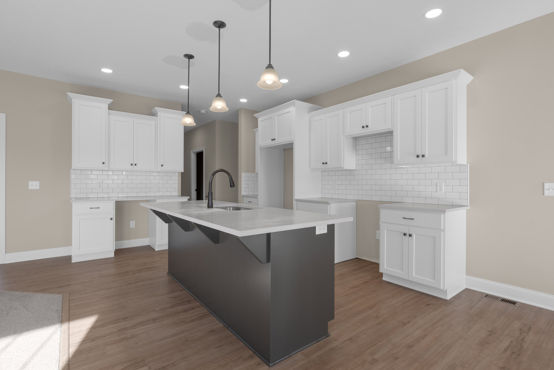 White kitchen cabinets with white countertops, black island featuring built-in sink, pendant light fixtures, light hardwood flooring, and subtle shadows across a white rug.