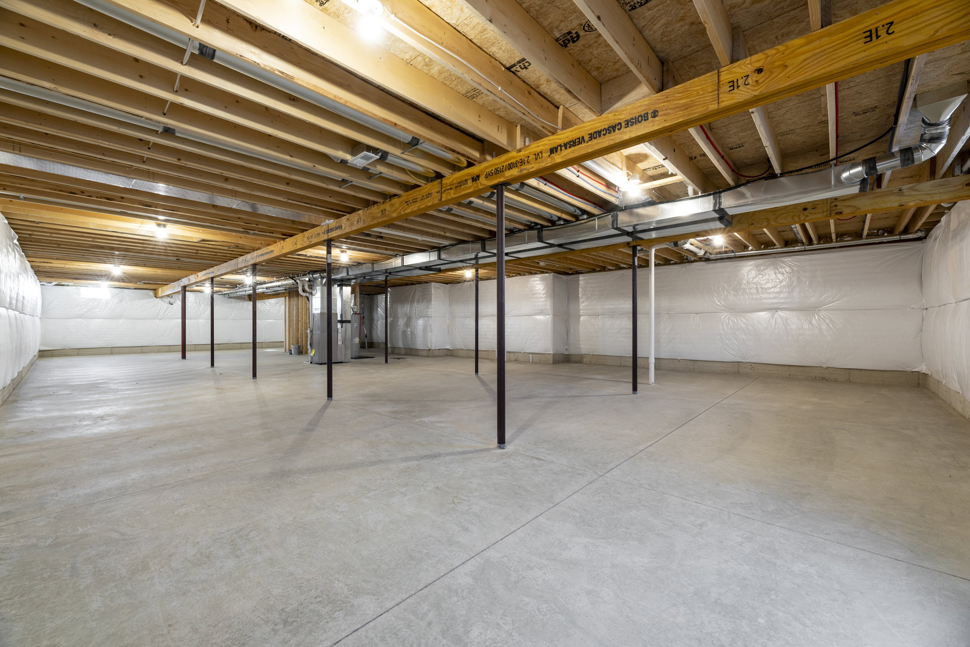 Open room with exposed wooden ceiling beams, concrete floor, black metal support poles, and unfinished walls