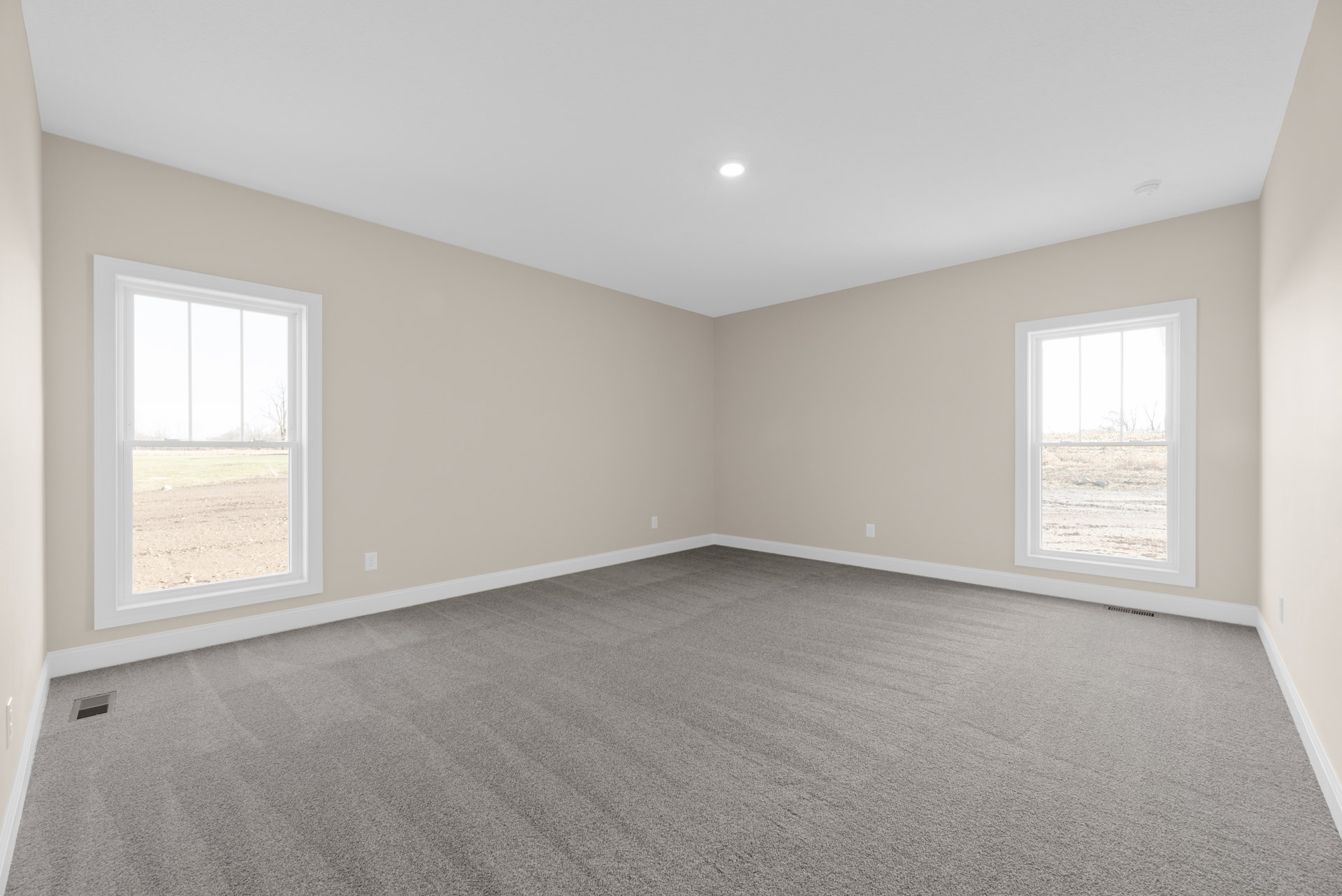 Carpeted room with multiple windows, white walls, ceiling light fixture, and view of grassy field outside