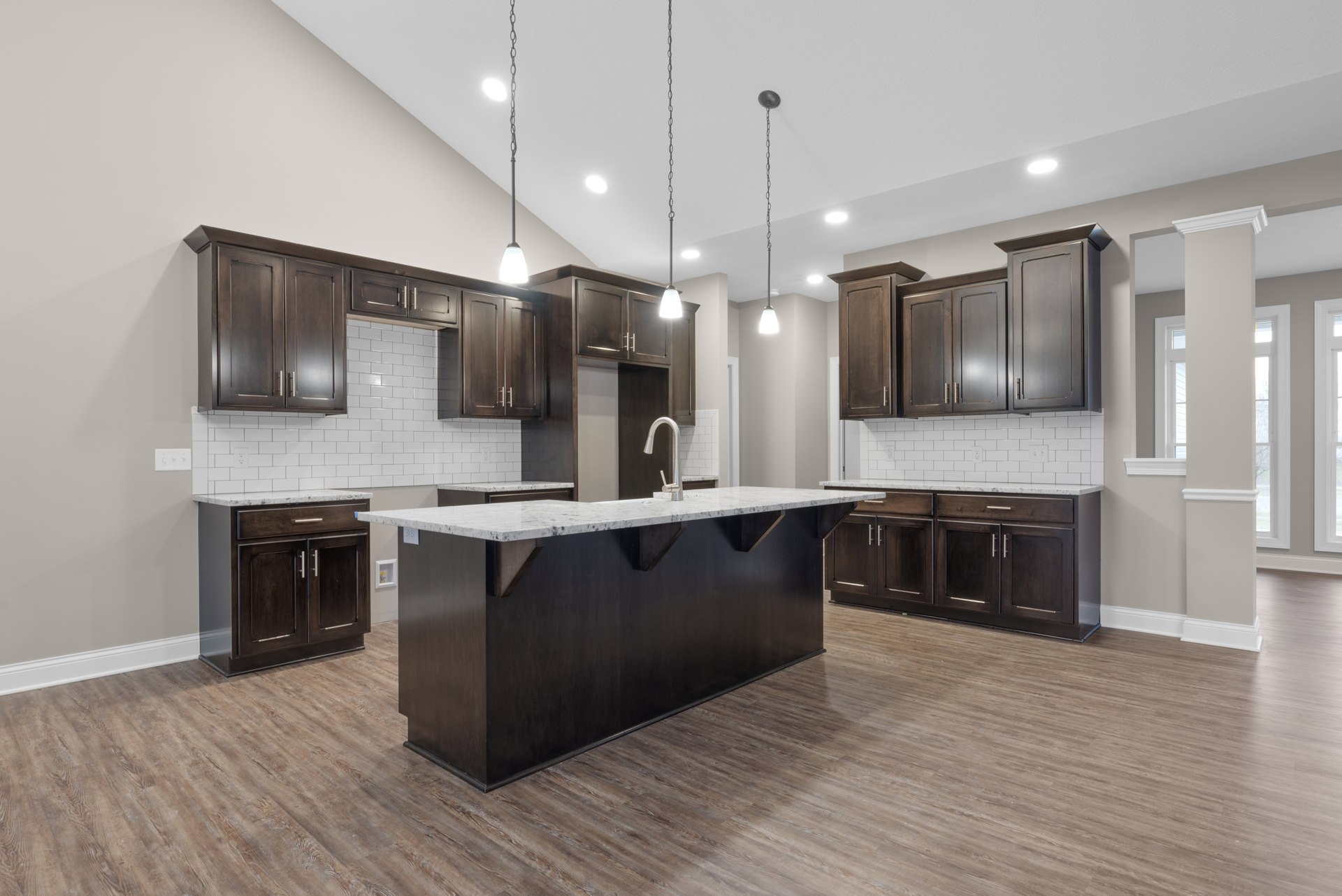 Dark wood kitchen cabinets with white marble countertop, stainless steel sink, light wood flooring, and neutral wall.