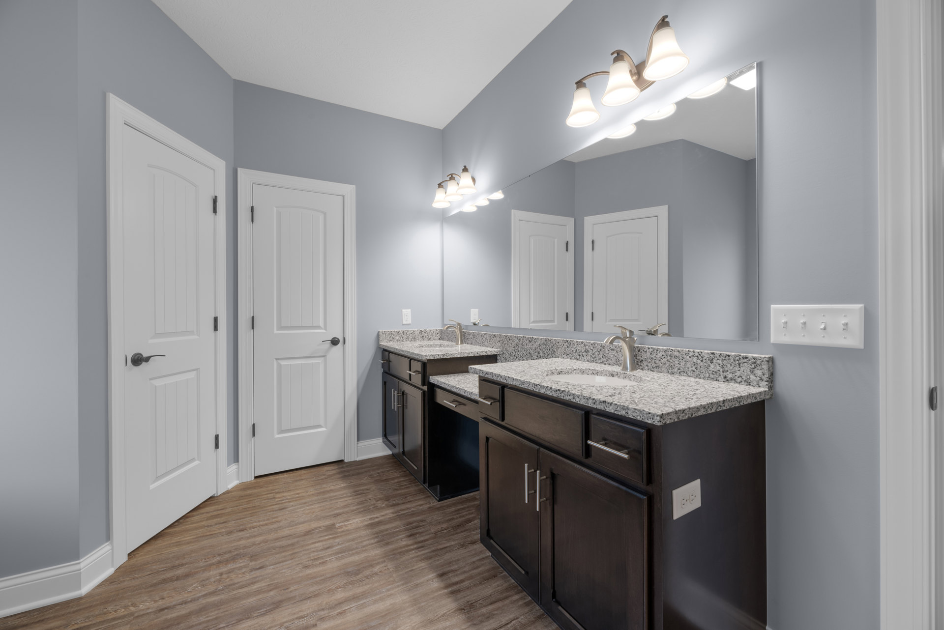 Bathroom with two rectangular sinks set in a white countertop, large frameless mirror above, white cabinetry below, black hardware on doors and drawers, three-light fixture mounted