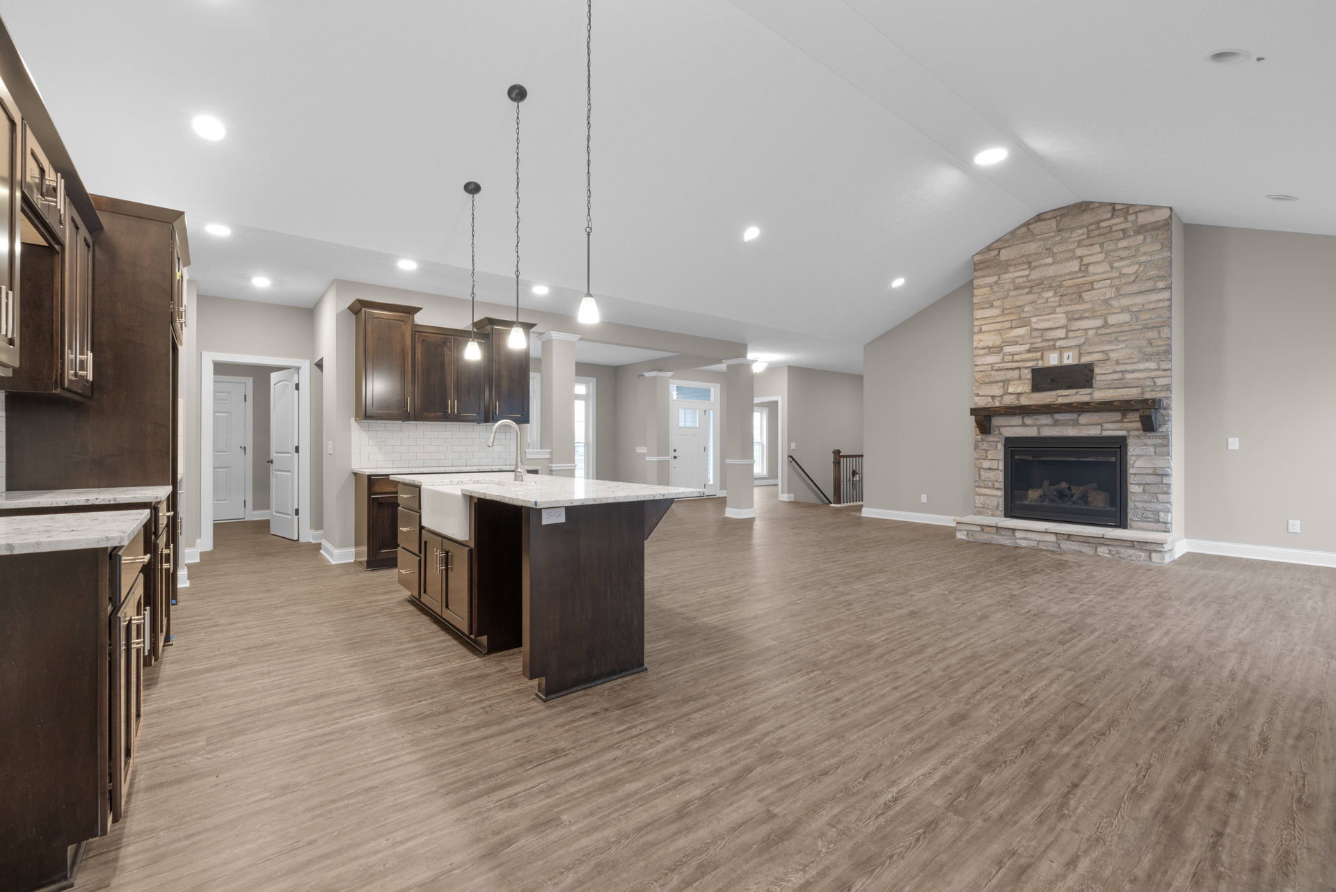 Spacious open floor plan featuring laminate flooring, marble kitchen island with sink, wood cabinetry, fireplace with log set and wood mantel, recessed ceiling lighting