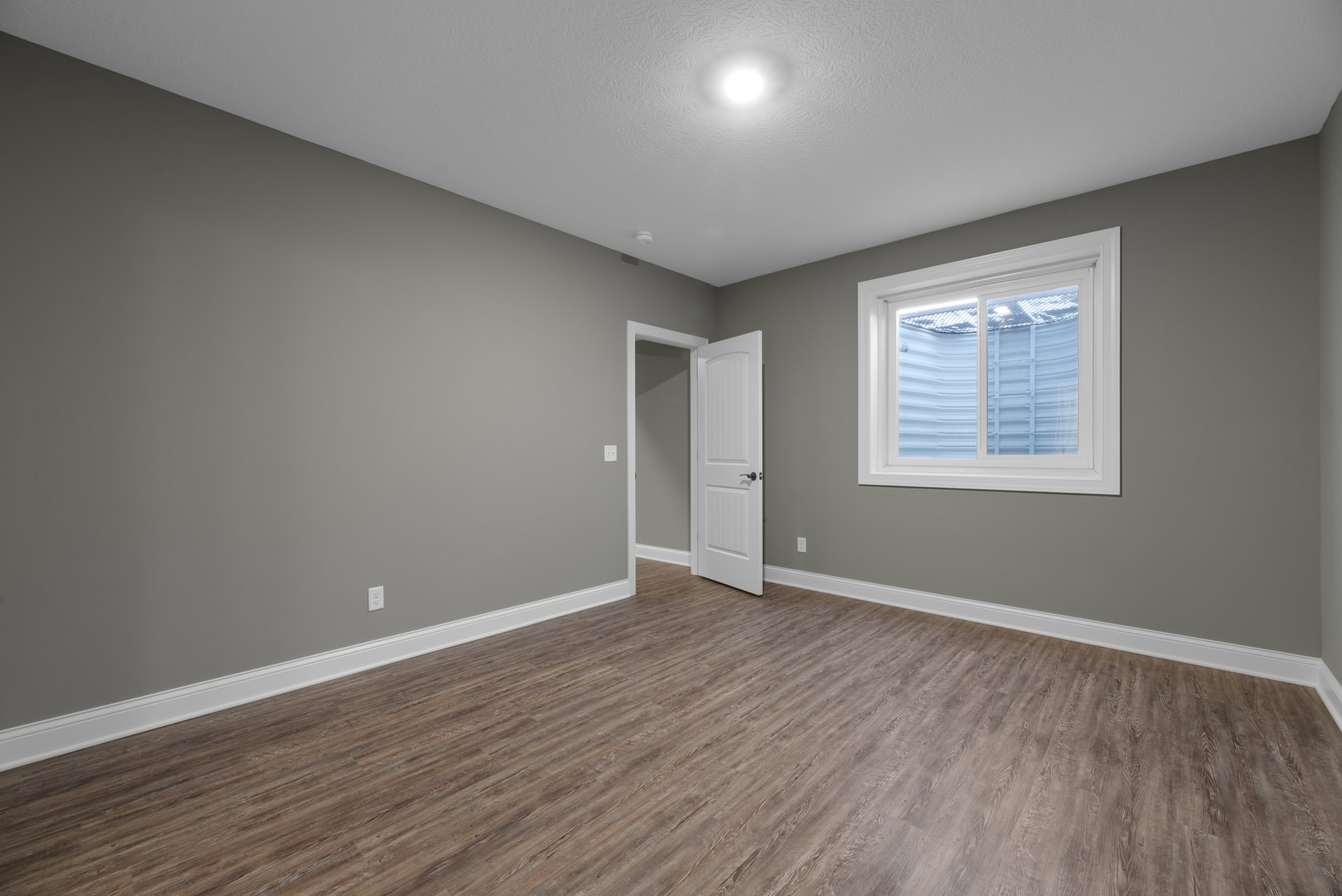 White-framed window, open white door, wood laminate flooring, plaster walls, ceiling light fixture