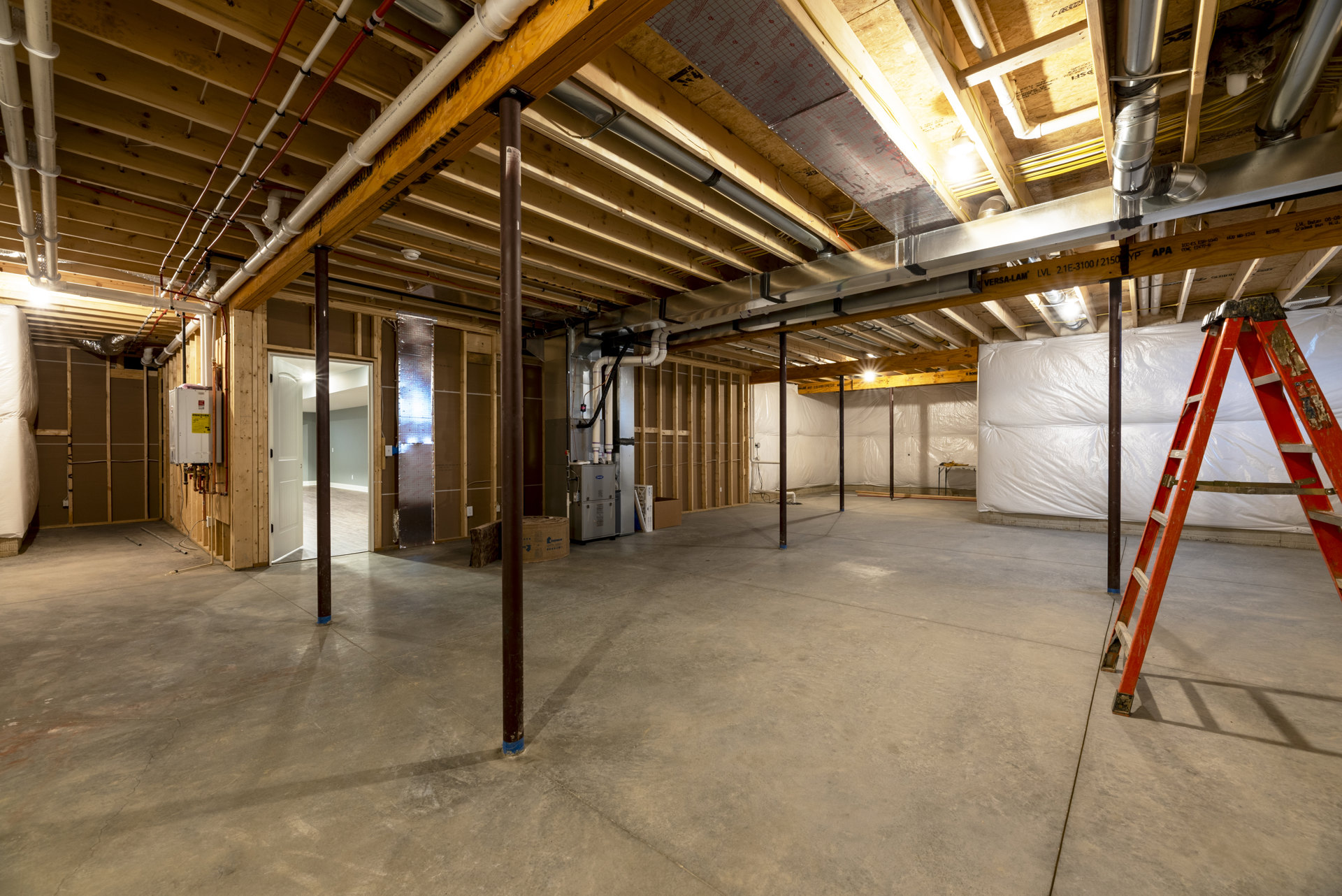 Concrete floor with exposed metal beams, unfinished ceiling, and a ladder leaning against a structural pole in a residential interior under construction