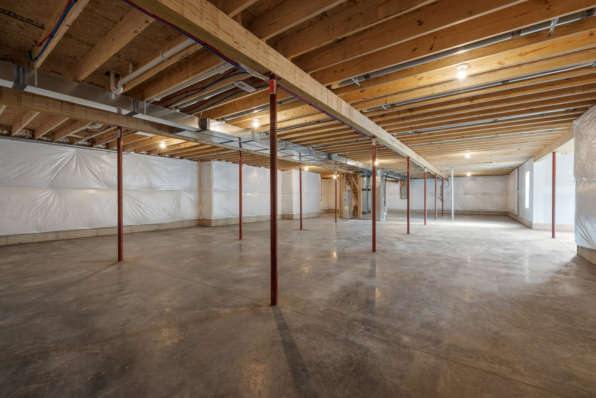 Exposed wooden ceiling beams with visible pipes, concrete floor supported by red poles, scattered white sheets of paper, and unfinished walls in an indoor room