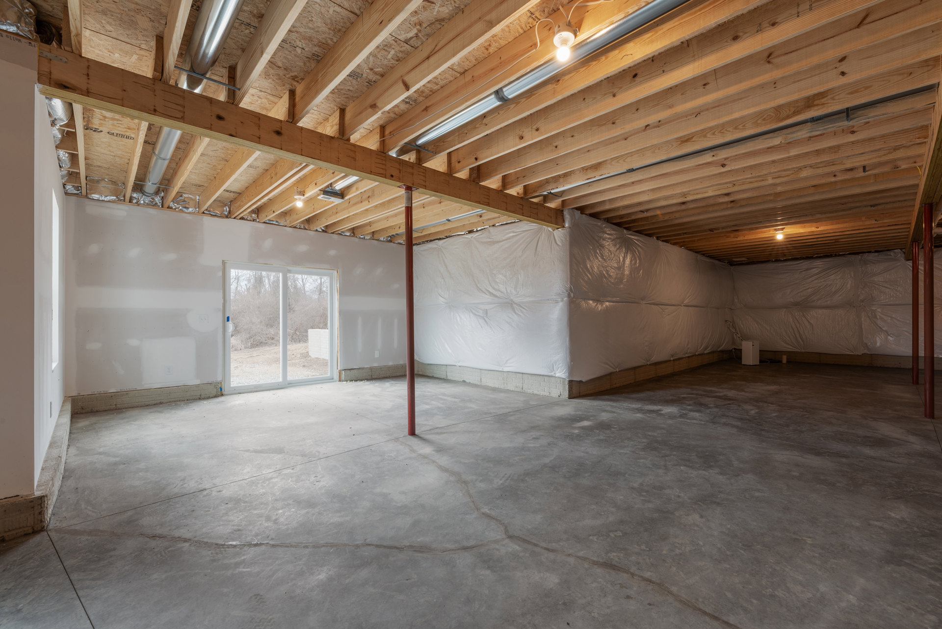 White plaster wall and ceiling, concrete floor with red support pole, window overlooking field of bare trees, ceiling light fixture.