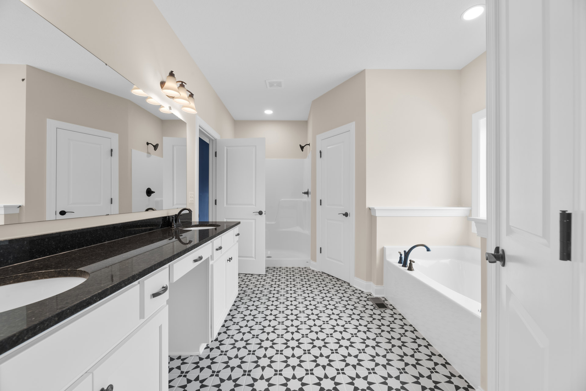 Bathroom with black and white tiled floor, white tile walls, white door featuring black handles, ceiling light fixture with multiple bulbs, white cabinetry, and countertop sink.