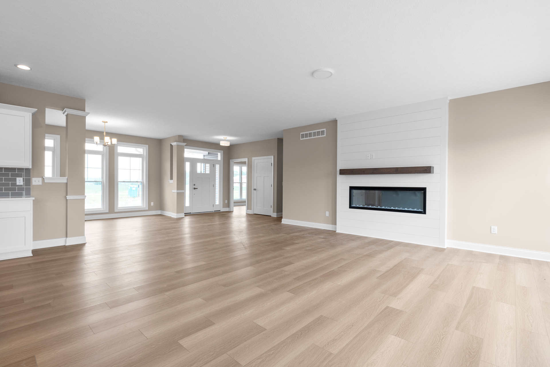 Spacious empty room with hardwood flooring, white walls, central fireplace, large window, and white door with silver handle