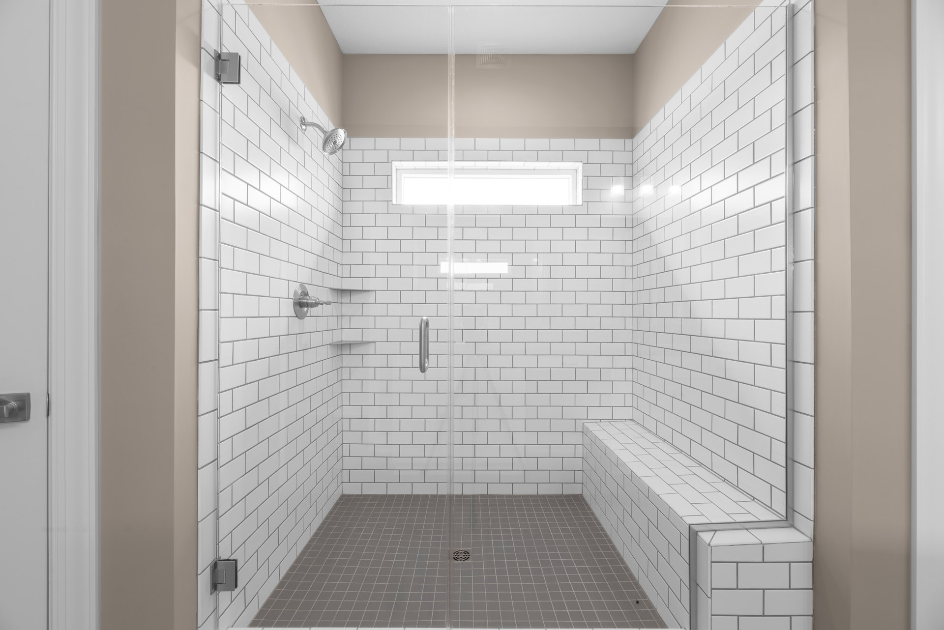 Frameless glass shower enclosure with silver handle and hinge, white tile walls, built-in drain, and chrome shower head