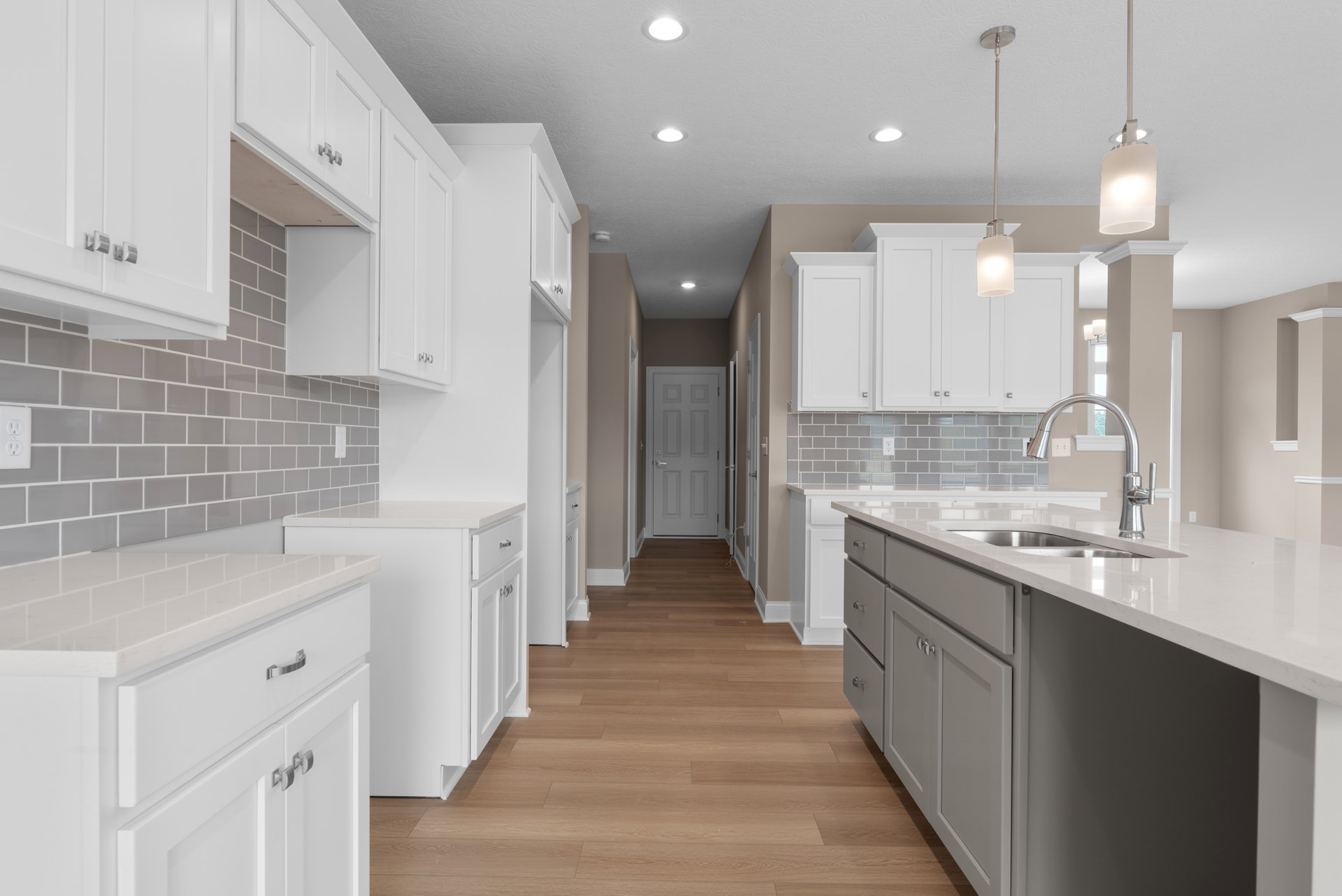 White kitchen cabinets with silver handles, wood plank flooring, white countertop, stainless steel sink, and a modern light fixture.