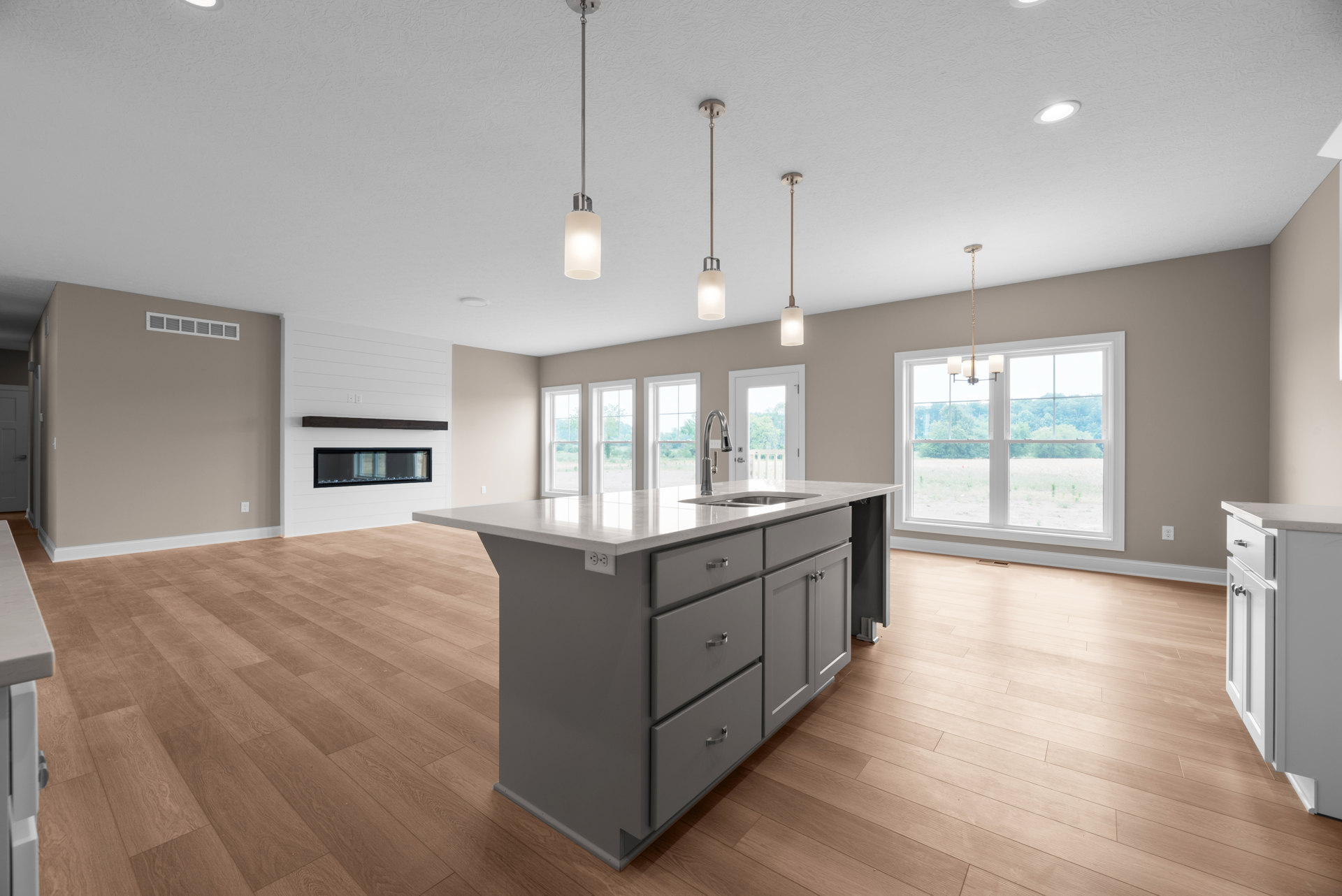 Spacious kitchen featuring a large white island with built-in sink and drawers, pendant light fixture overhead, stainless steel faucet, white cabinetry, and a window providing