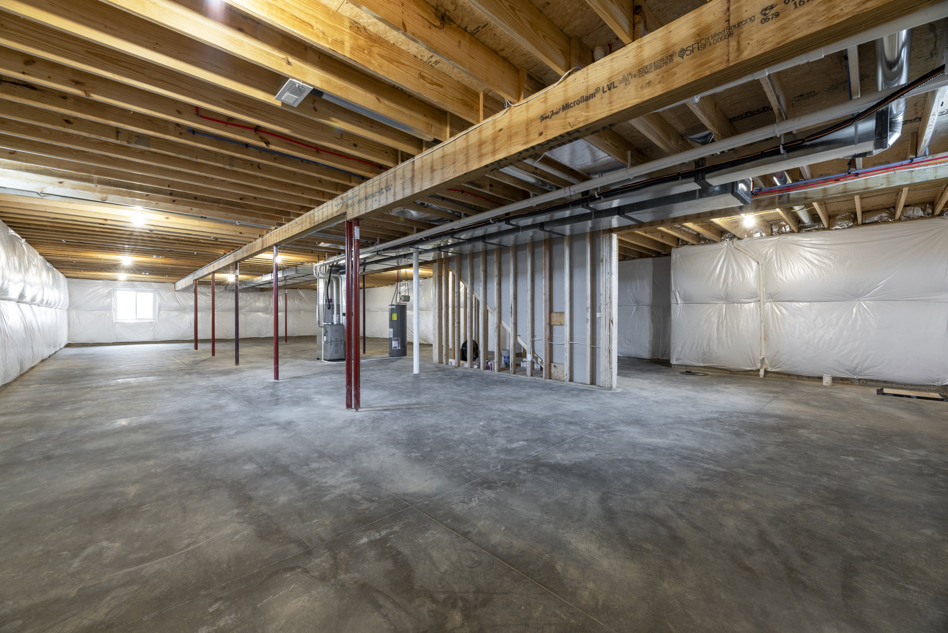 Concrete floor with a red support pole, exposed wood and metal ceiling beams, white plastic wall covering, ceiling vent, and close-up of a white bed