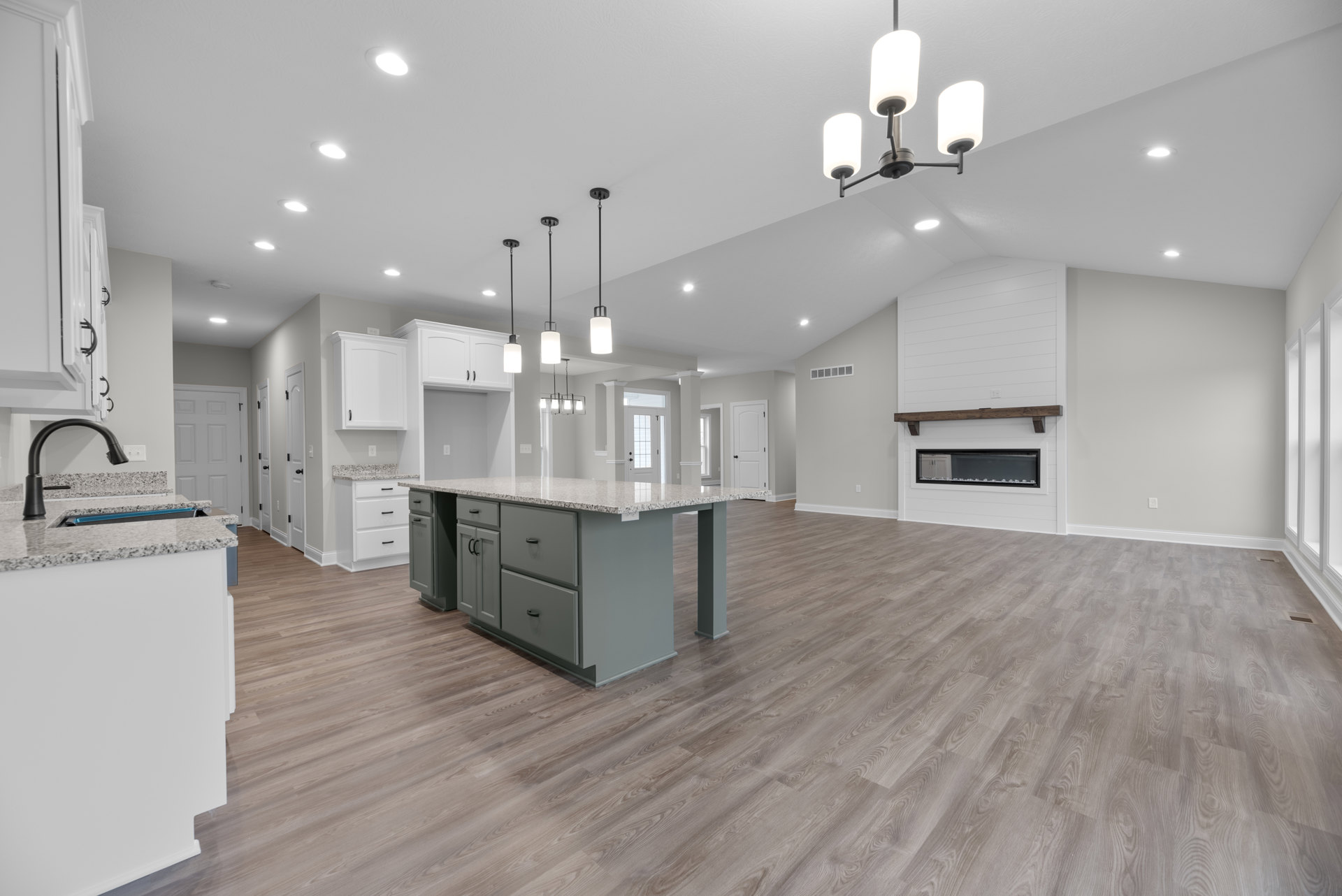 Open-concept kitchen with wood flooring, white cabinetry, large central island, pendant light fixture, and modern fireplace against a blue accent wall