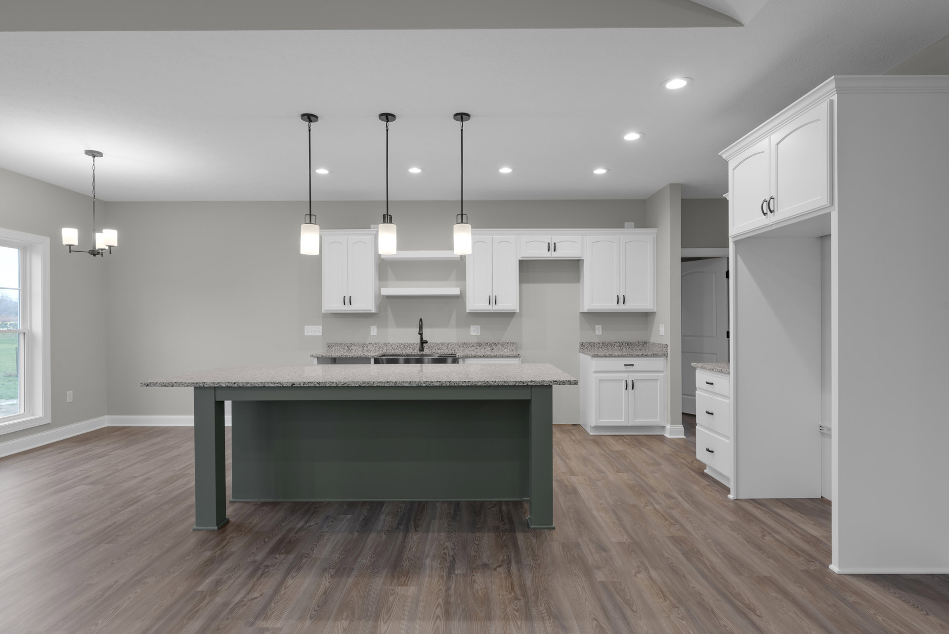 Kitchen with white shaker cabinets, central island with granite countertop, stainless steel sink, wood flooring, and large window above the counter.