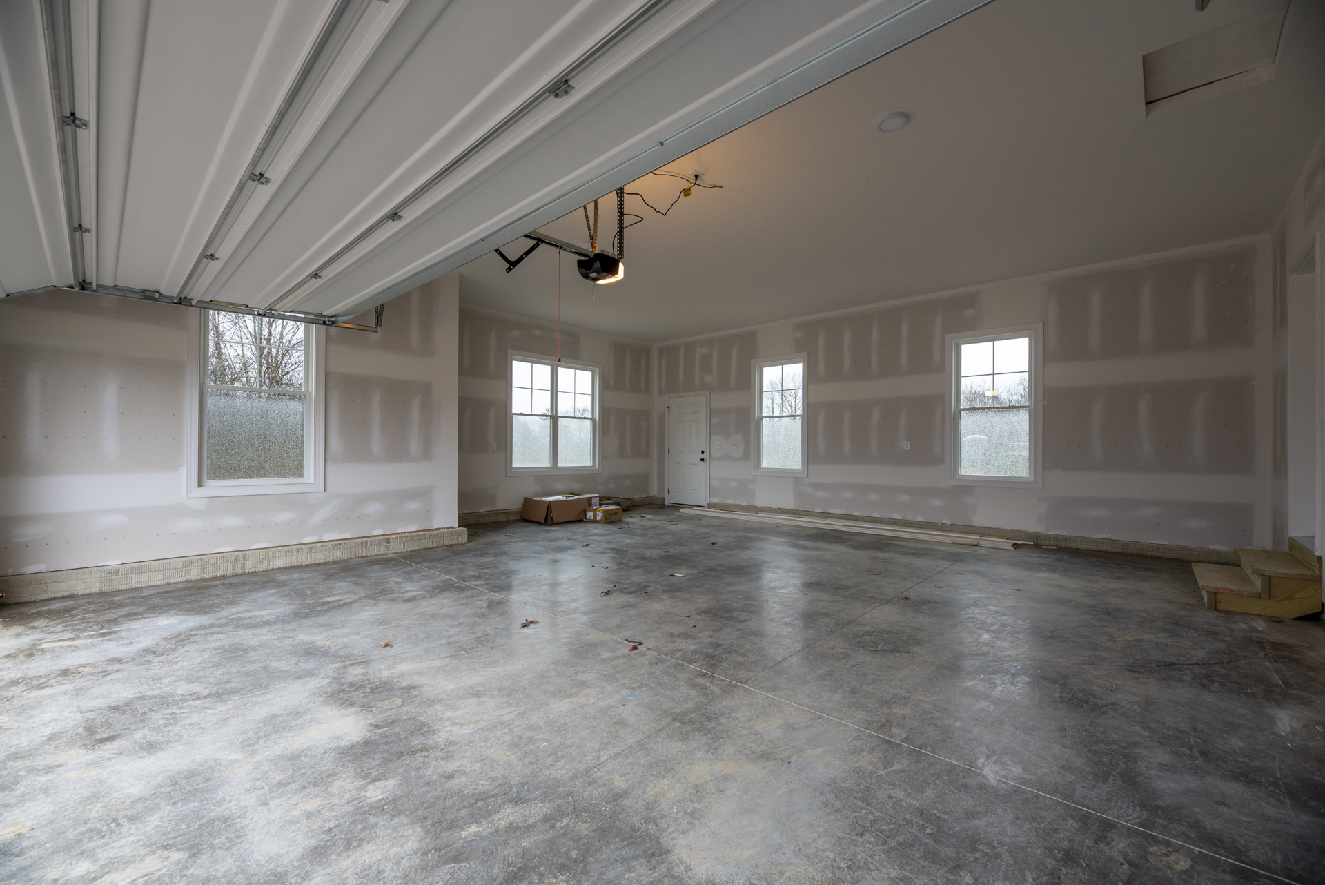 Concrete-floored room with multiple windows, including one with frosted glass and another with a red object visible outside; boxes scattered on the floor, yellow and black cable
