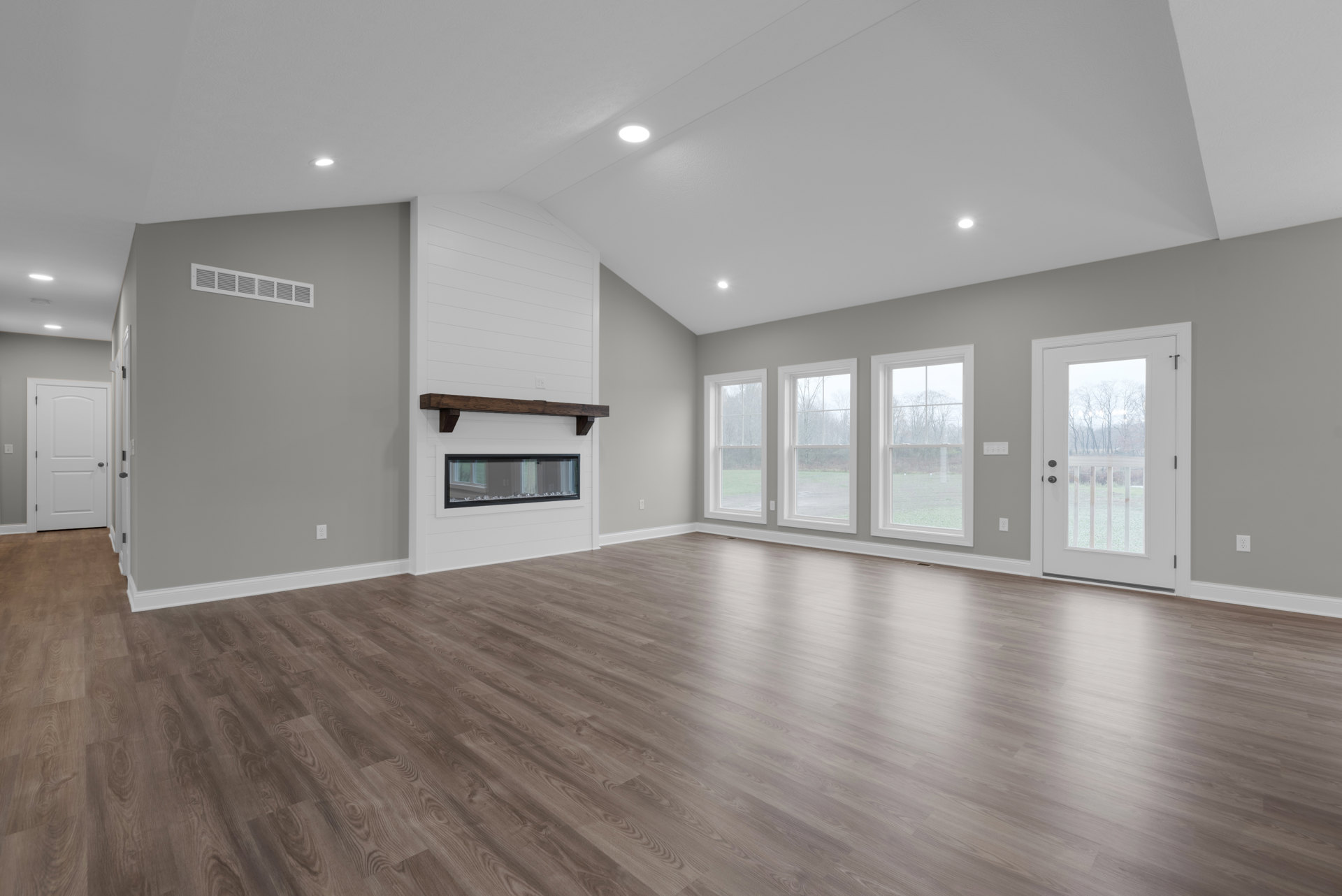 Spacious living area with hardwood floors, central fireplace, large window overlooking trees, white door with black handle, and black-framed glass door