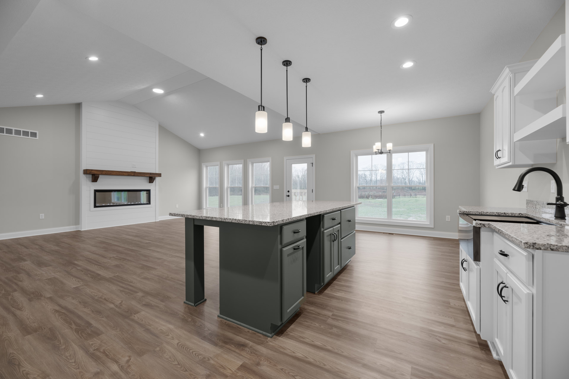 Spacious kitchen featuring a marble-topped island, wood flooring, white cabinetry, recessed ceiling lights, stainless steel appliances, and a window overlooking a grassy field