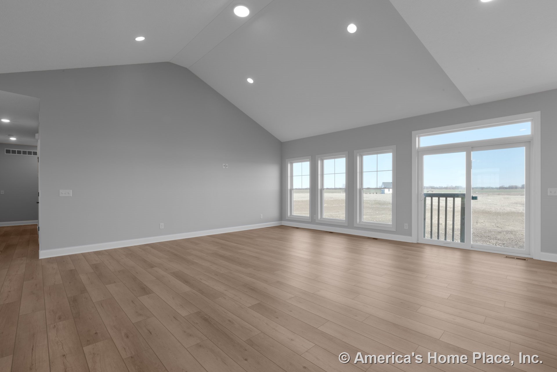 Vaulted ceiling living room with recessed lighting, wide plank wood flooring, expansive window wall, sliding glass door, white baseboard trim, and gray walls showcasing modern