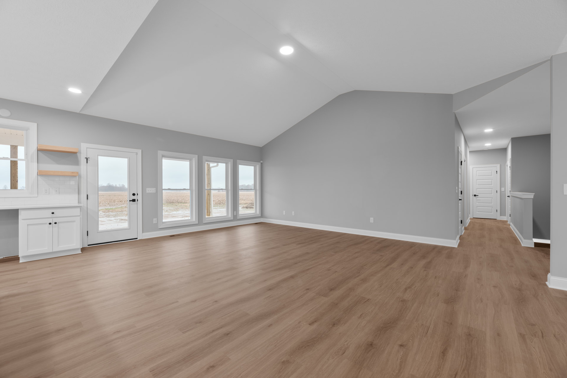 Hardwood floor room with white walls, large windows overlooking a grassy field, white door with black handle, ceiling light fixture