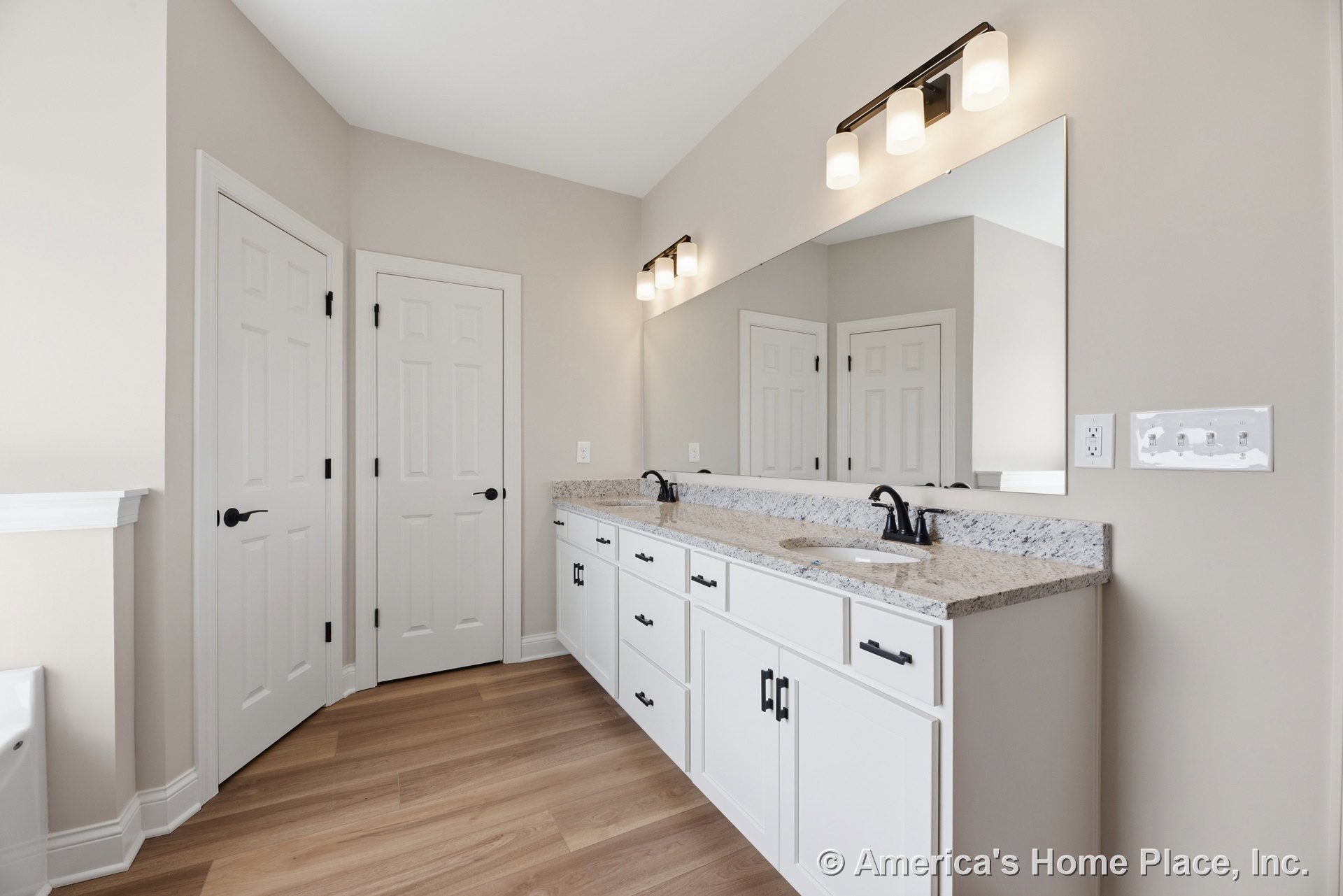 Double sink vanity with granite countertop, white shaker cabinets, large wall mirror, modern vanity lighting, wood-look flooring, white trim, and contemporary hardware.