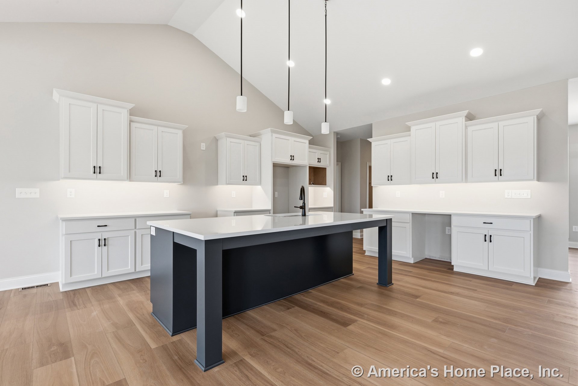 White shaker cabinets with matte black hardware, navy kitchen island featuring a waterfall-edge quartz countertop, pendant lights suspended above the island, light wood plank