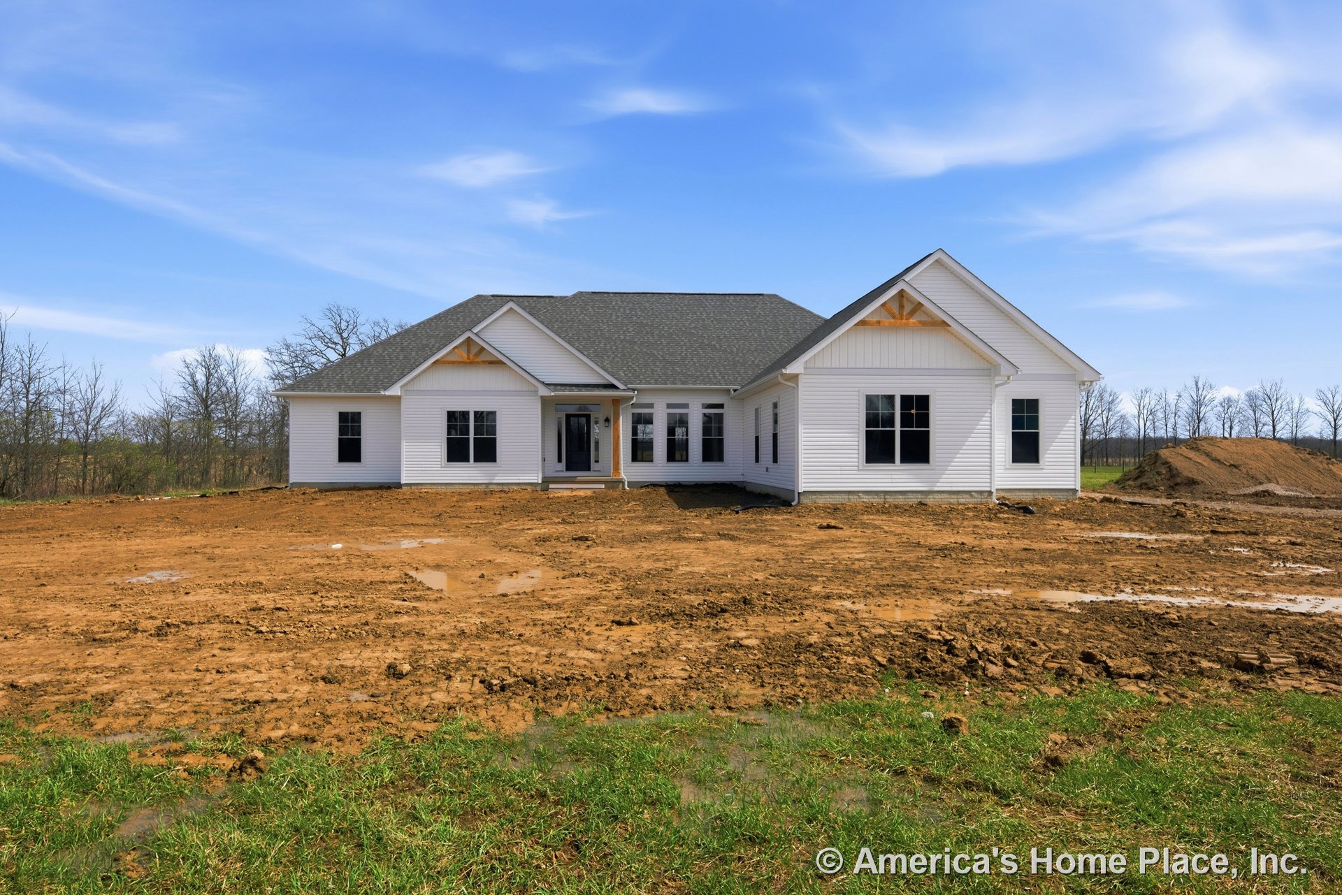 White horizontal siding and dark shingle gable roof with wood trim accents; covered front porch and multiple large rectangular windows; unfinished yard in front of new construction