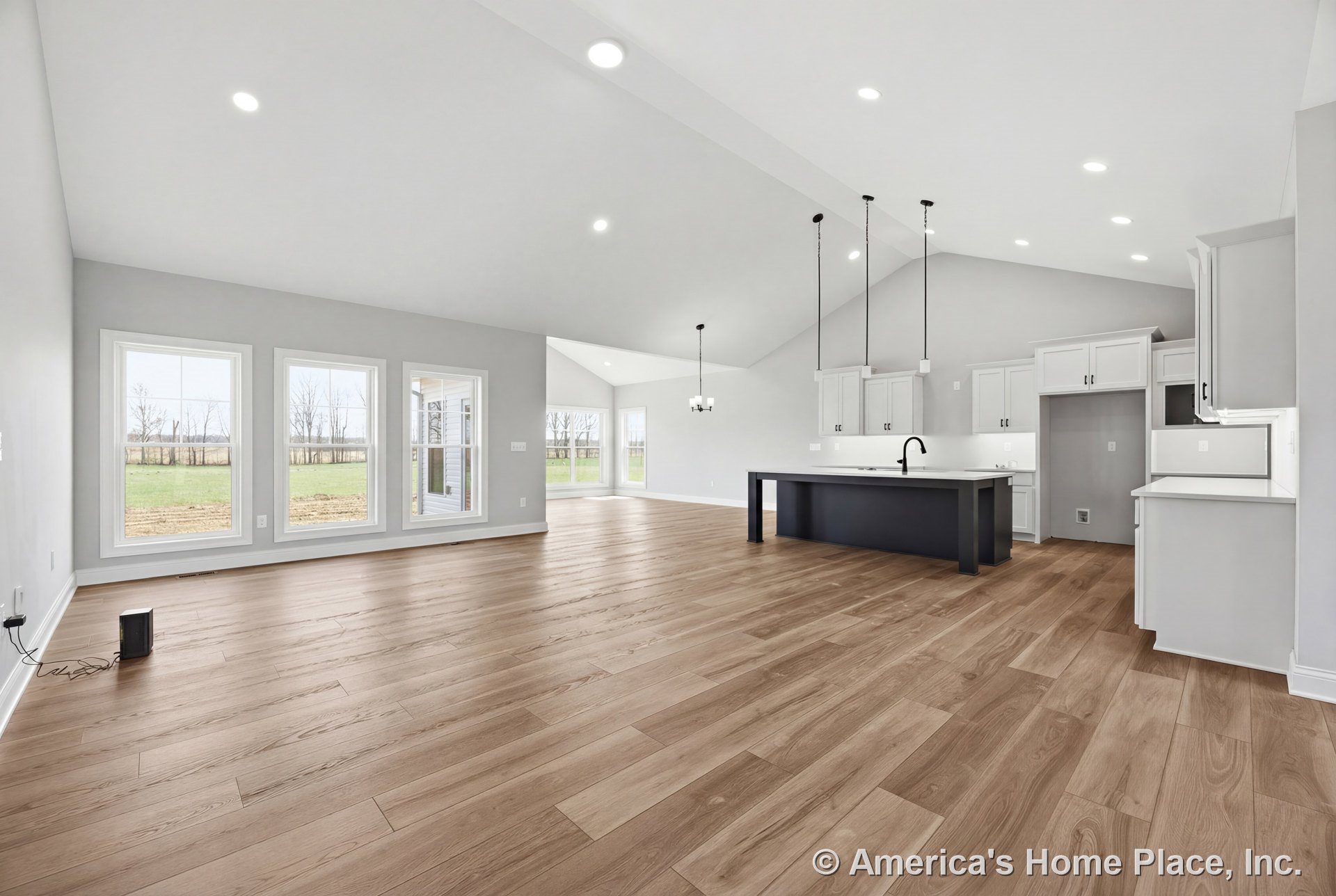 Open-concept kitchen and living area with vaulted ceiling, recessed lighting, wide plank wood flooring, three large picture windows, white shaker cabinets, dark kitchen island with