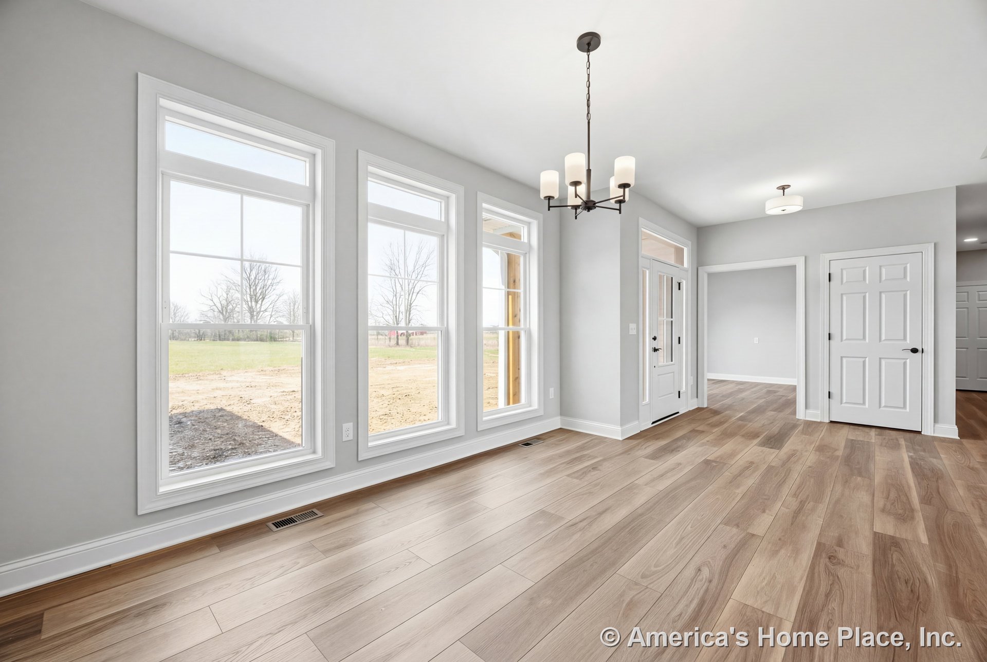 Foyer with three tall picture windows, light wood plank flooring, white baseboards and trim, modern chandelier, white paneled doors, and transom window above entry door.