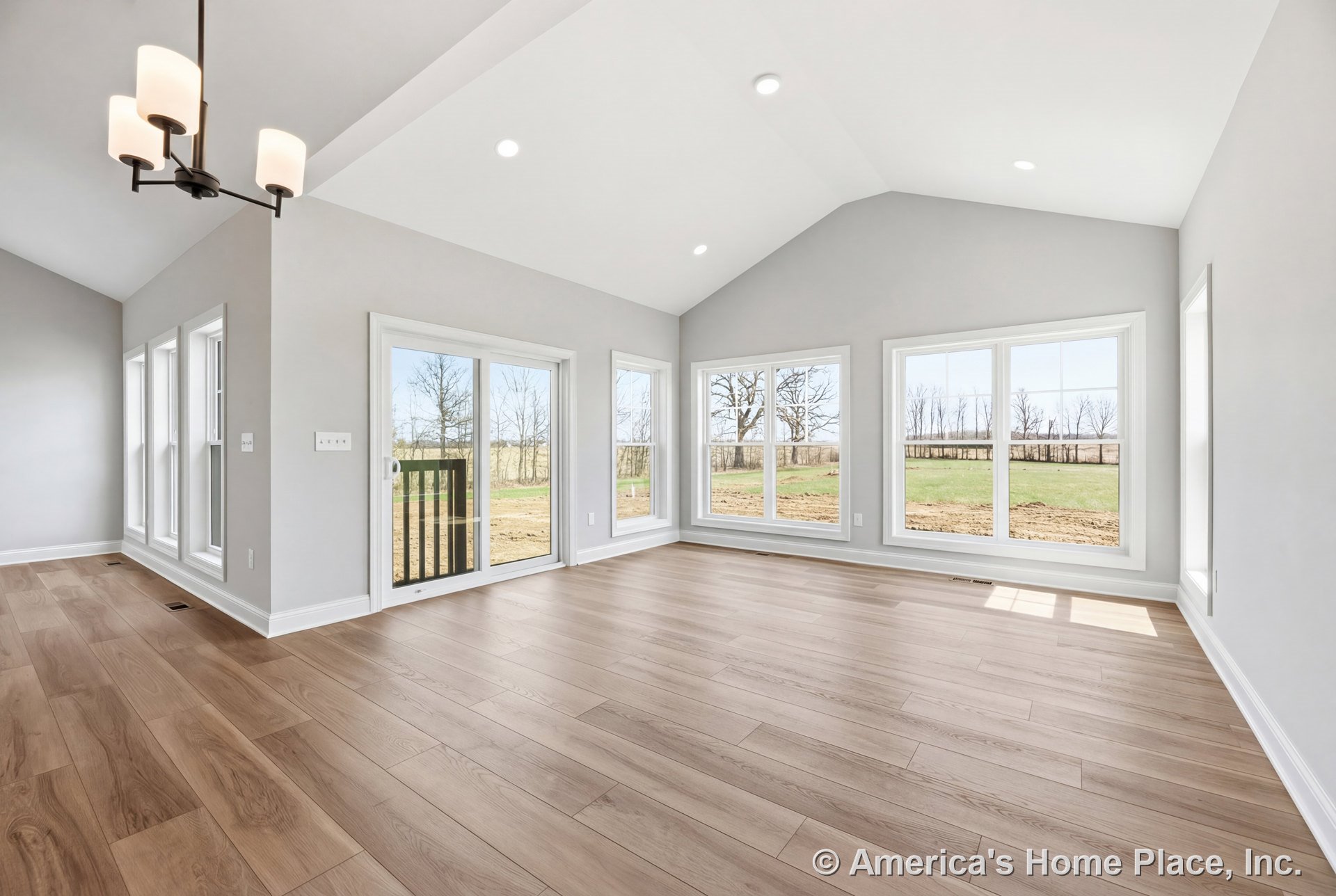 Wide plank light wood flooring, vaulted ceiling with recessed lighting, expansive window wall, sliding glass door, modern chandelier, white trim, and open layout in the living