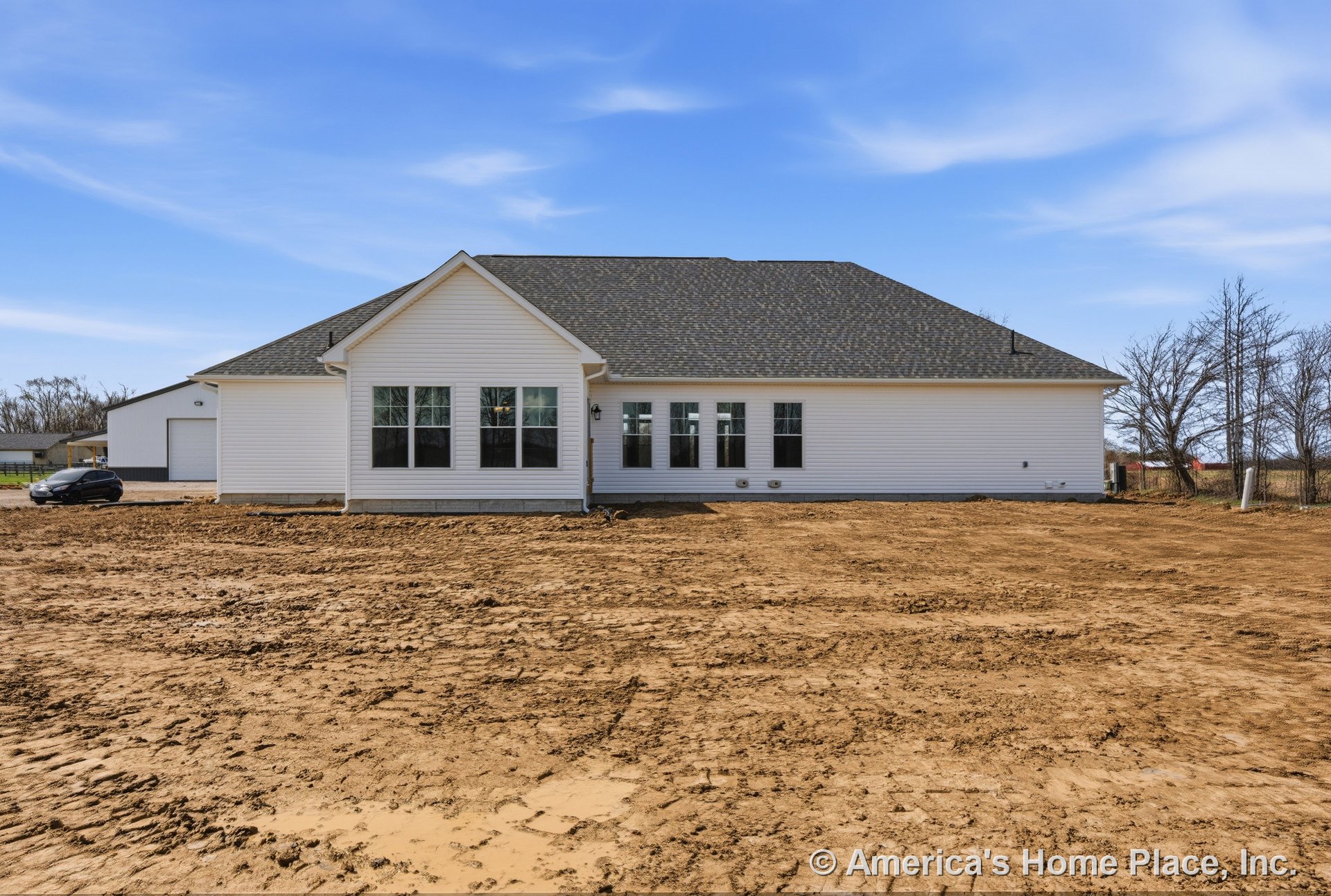 White vinyl siding single-story home with gable roof, black shingles, multiple large windows, exterior wall light, and unfinished yard.