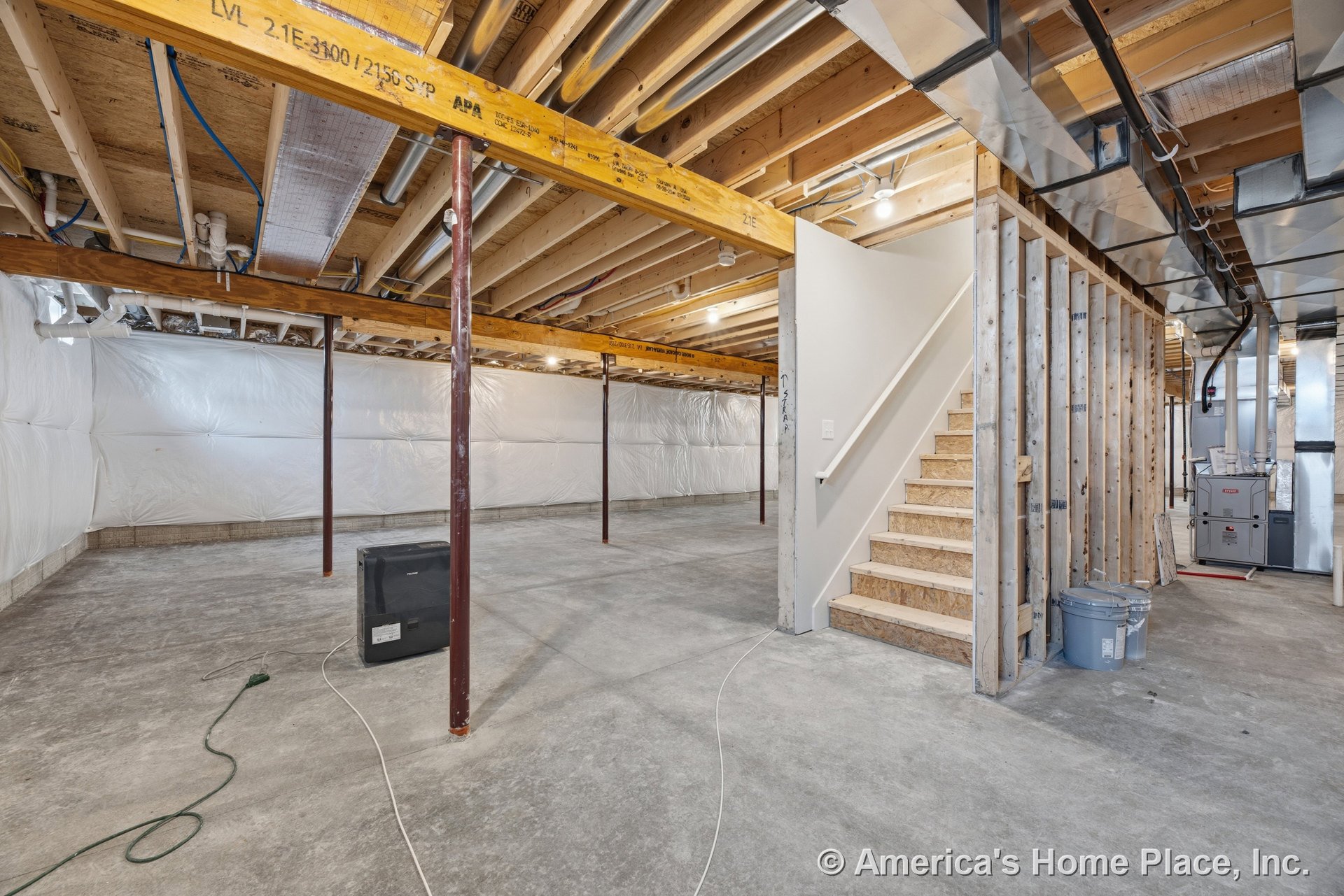 Exposed wood ceiling joists, concrete floor, unfinished staircase, plastic wall insulation, metal support columns, and utility furnace in spacious unfinished basement.