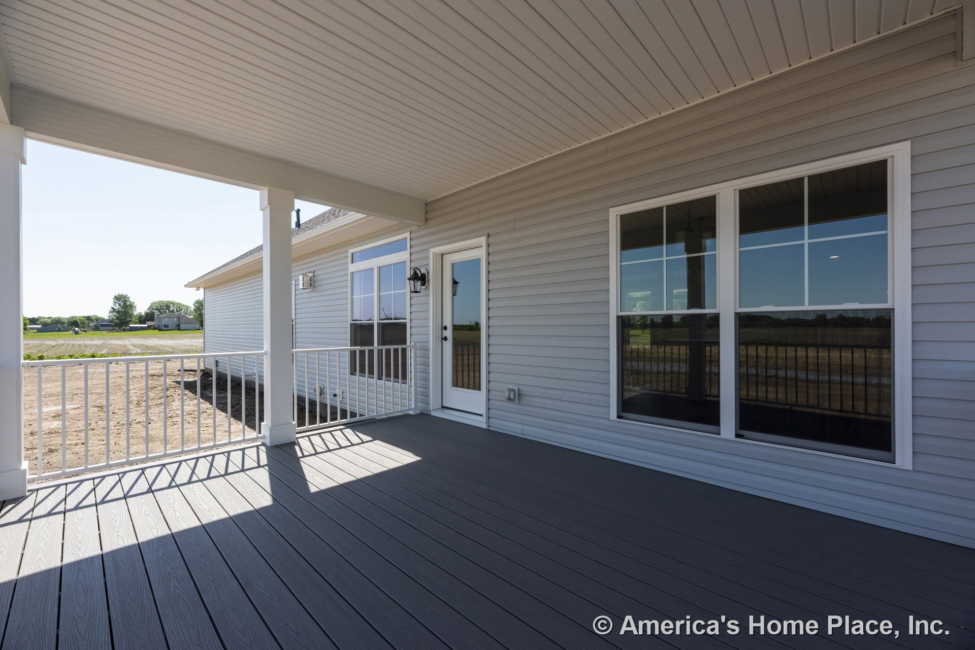 Covered back porch with gray composite decking, white metal railings, double-pane windows, glass exterior door, vinyl siding, beadboard ceiling, and permanent lighting fixtures.