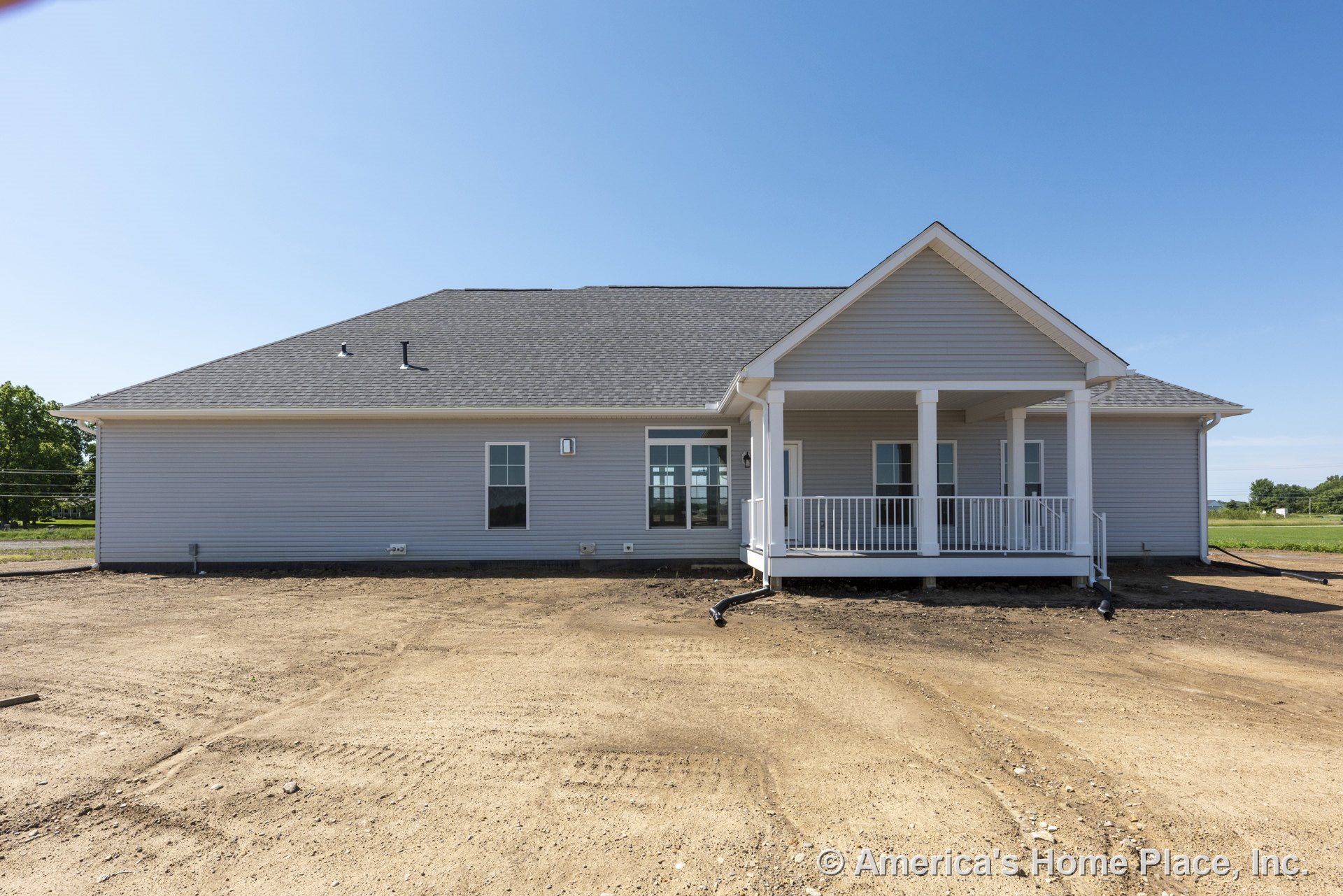 Gray vinyl siding exterior with gable roof, covered back porch supported by white columns and railings, multiple double-hung windows, and unfinished yard.