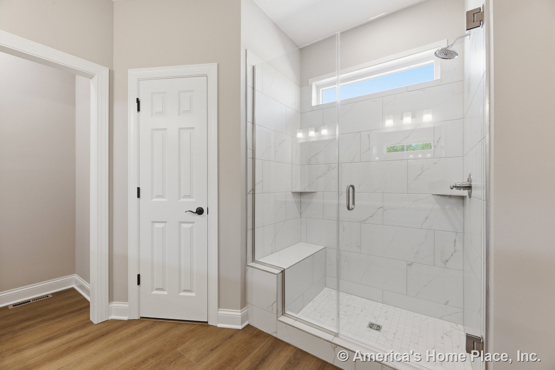 Walk-in shower with frameless glass enclosure, large marble-look tile, built-in bench, rectangular shower niche, and window above; white paneled interior door, wood-look flooring