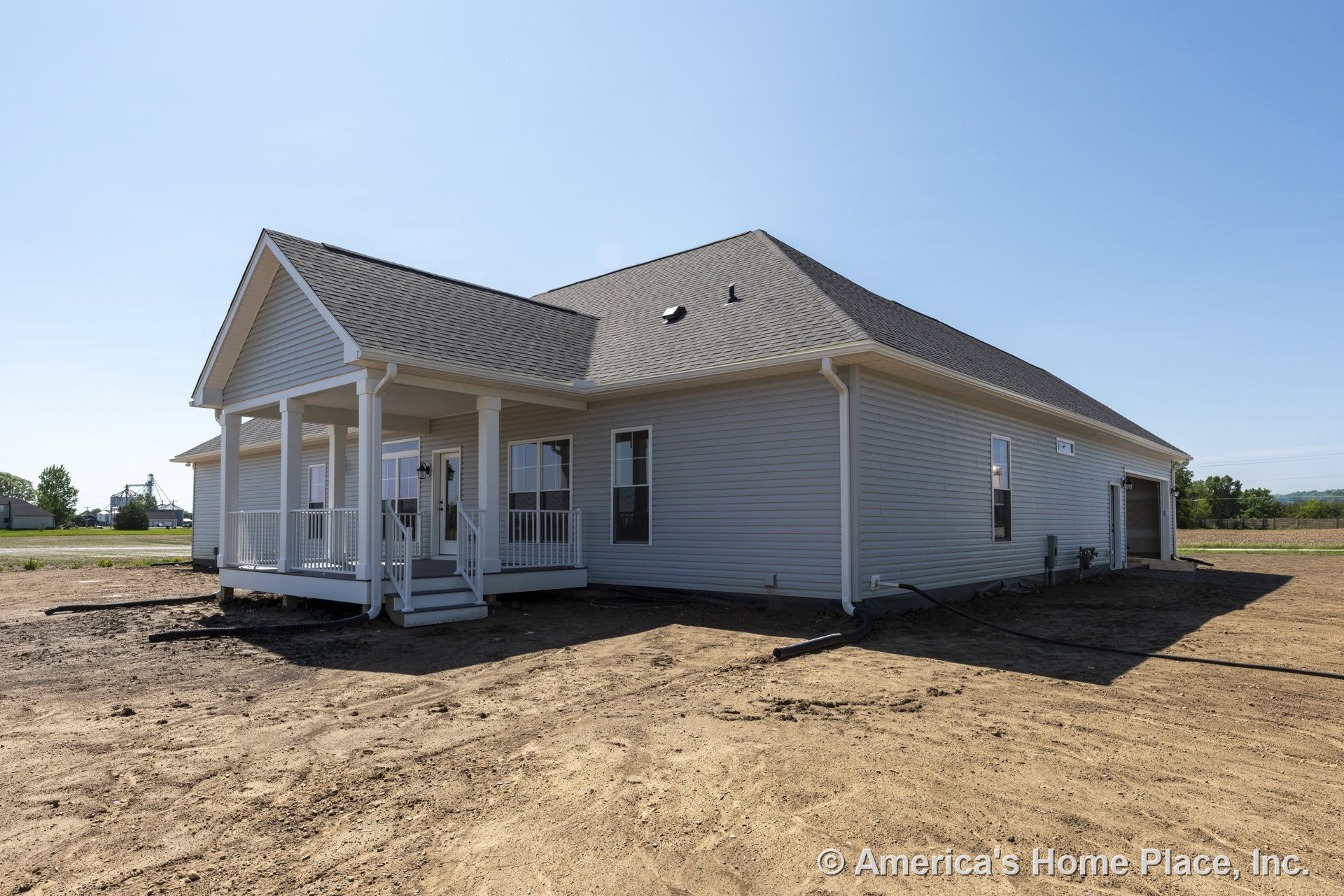 Covered front porch with white railings and columns, vinyl siding exterior, hip roof with asphalt shingles, multiple windows with white trim, attached garage, new construction