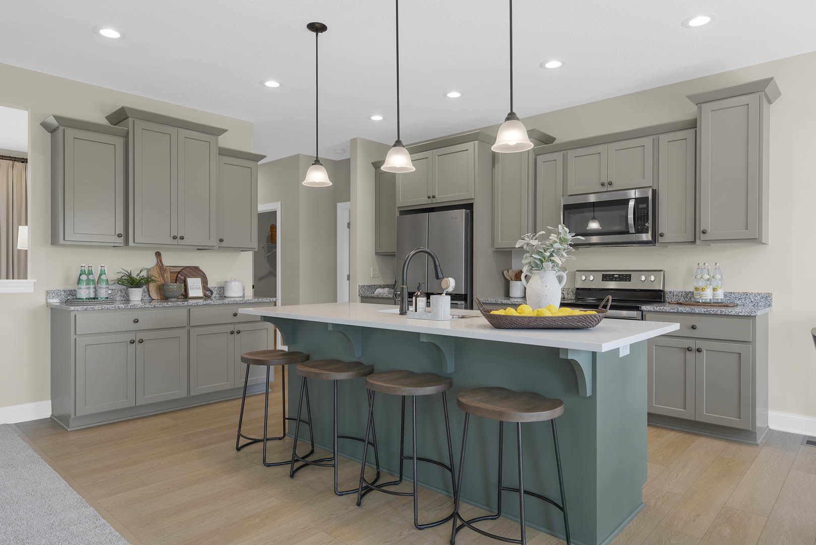 Modern kitchen featuring a central island with wooden stools, white cabinetry, stone countertops, stainless steel microwave, potted plant, and light wood flooring