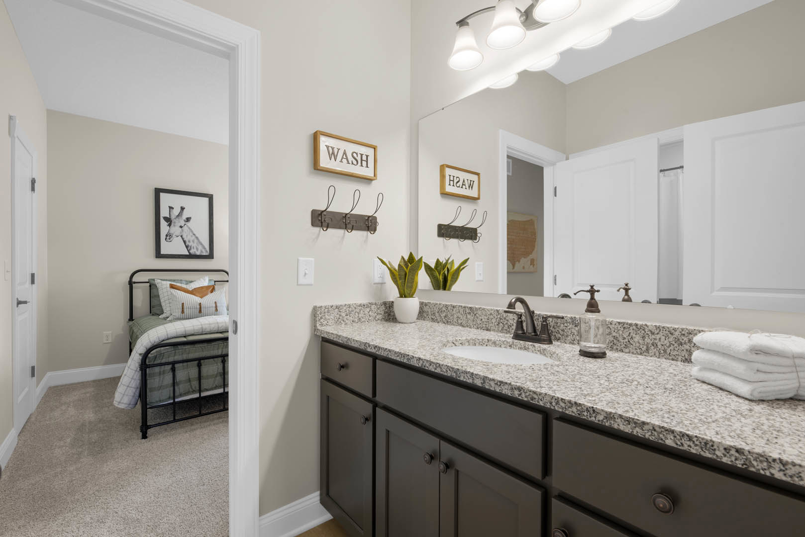 Modern bathroom with white tile walls, rectangular mirror above a sleek sink, wooden vanity with drawers, chrome faucet, stack of white towels, potted plant in a white pot, and