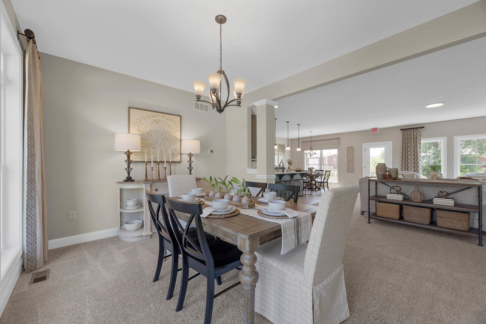 Wood dining table set with white plates and bowls, surrounded by chairs including one draped with a white cloth; built-in shelf holds baskets and books against neutral walls