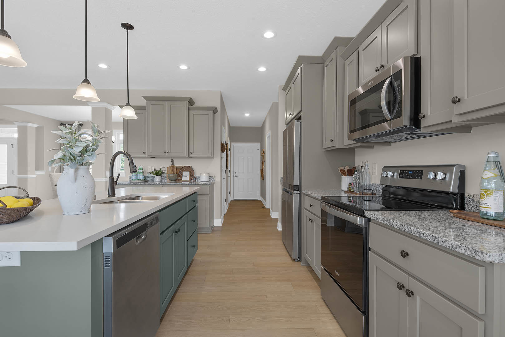 Kitchen with warm wood flooring, white cabinetry, stainless steel appliances, potted plant in a white pitcher on the countertop, basket of lemons, microwave oven, and a white door