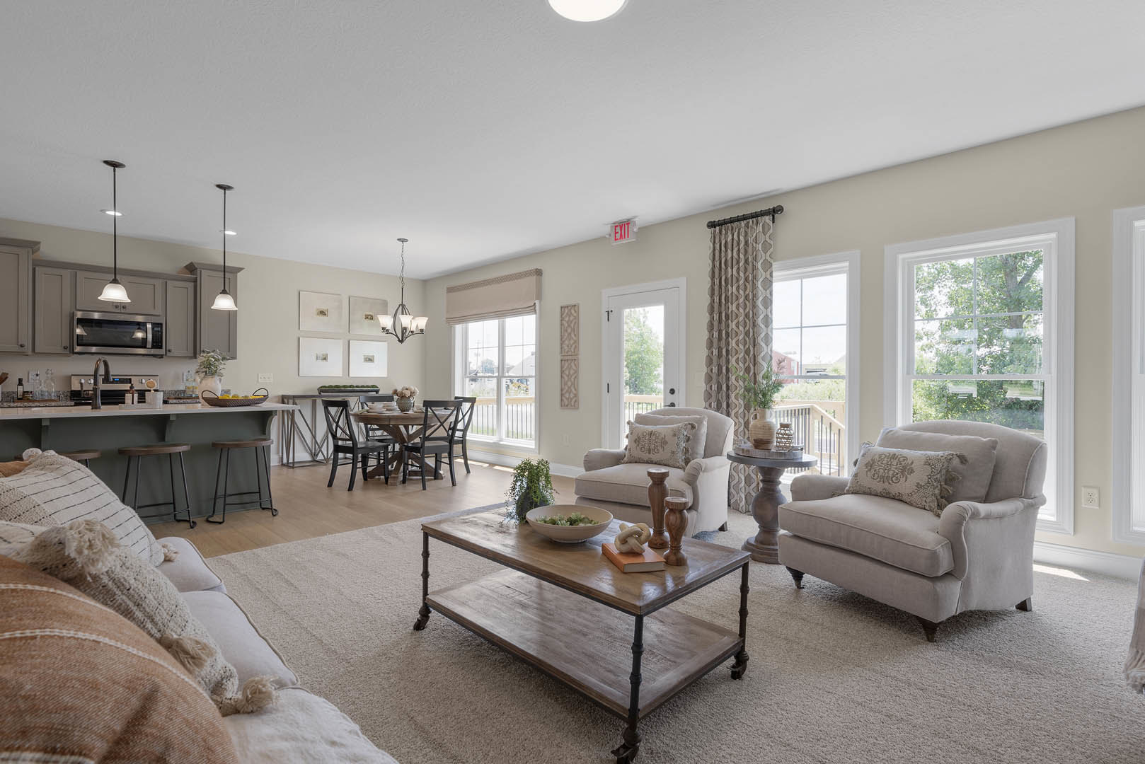 Living room with light wood floor, gray couch with patterned pillows, round coffee table holding a bowl, dining table and chairs, textured rug, neutral walls, and modern decor