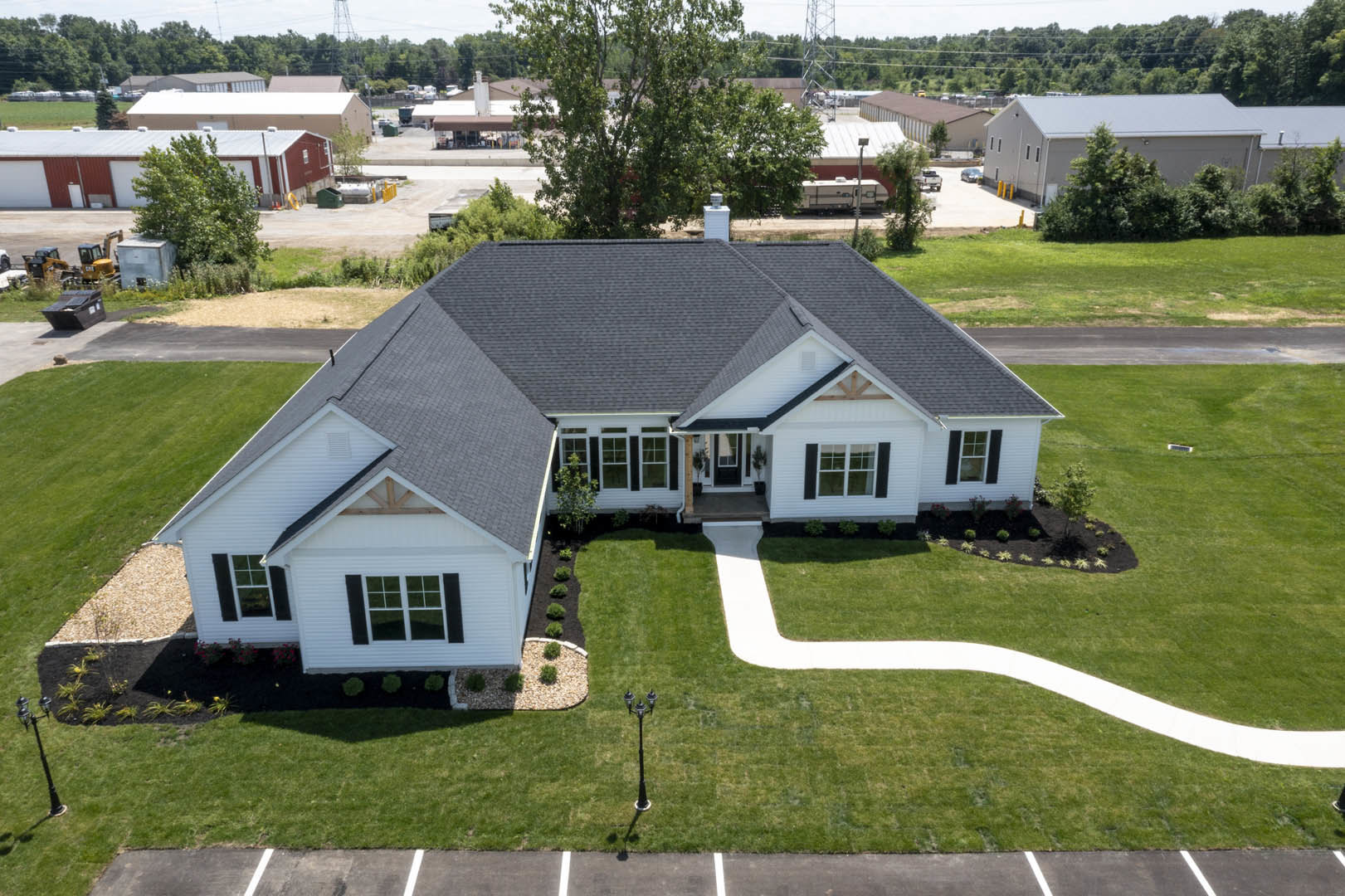 Two-story home with gray siding, white trim, large windows, concrete driveway, and green front lawn bordered by mature trees
